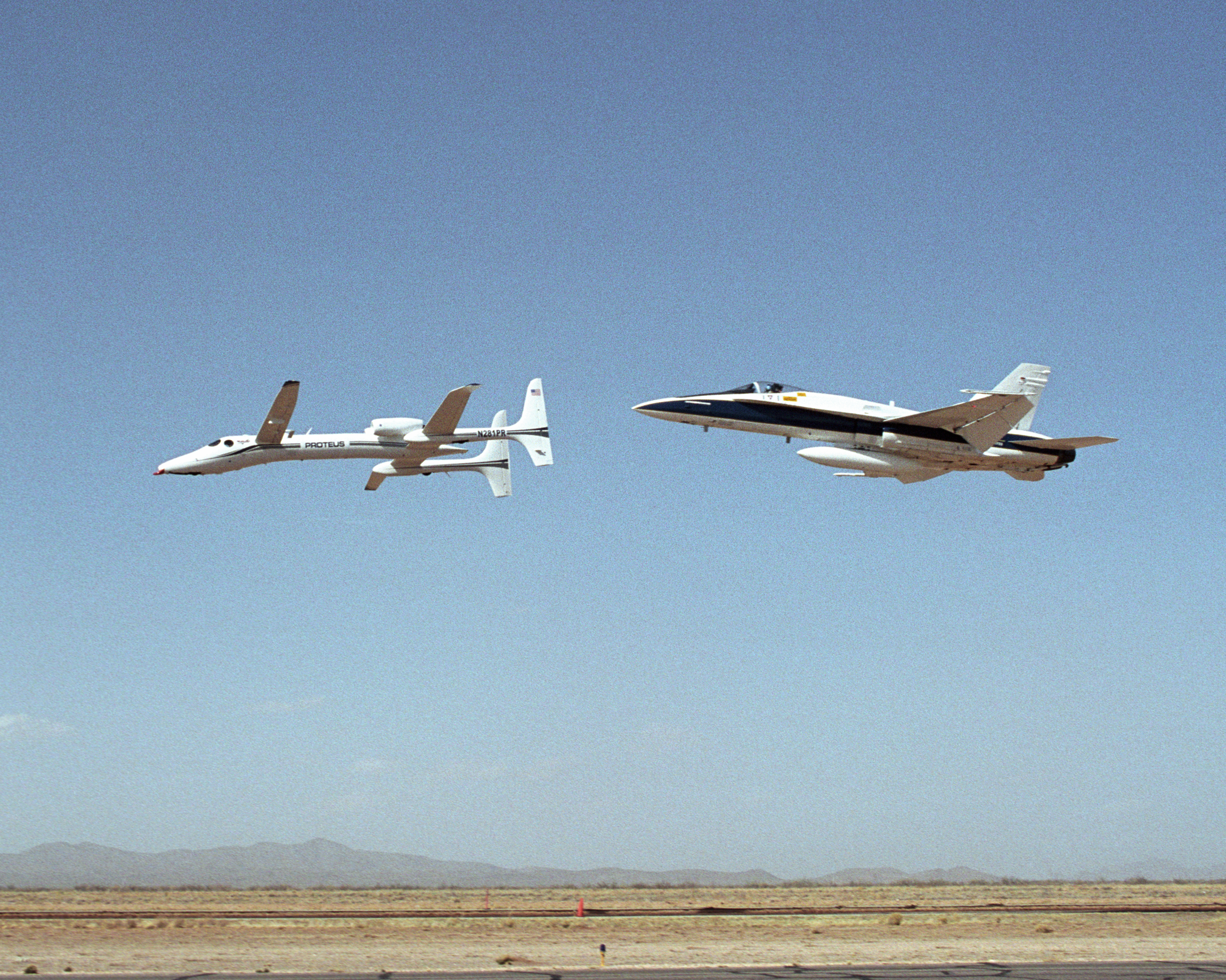 Scaled Composites' Proteus aircraft and an F/A-18 Hornet from NASA's Dryden Flight Research Center during a low-level flyby at Las Cruces Airport in New Mexico.