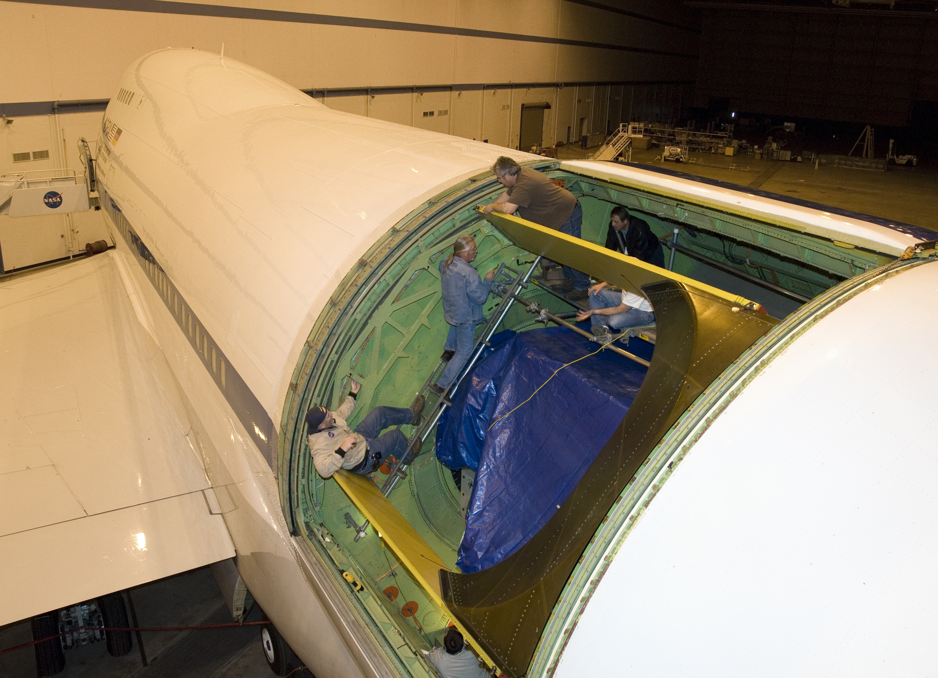 Technicians carefully disassemble portions of the aperture mounting assembly from NASA's SOFIA aircraft in preparation for removal of the telescope