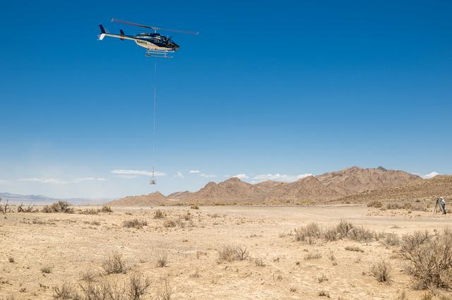 Blue and White Helicopter with a basket tethered on a cord below it, lifts off with the payload from Crater Island, Utah June 23, 2026.