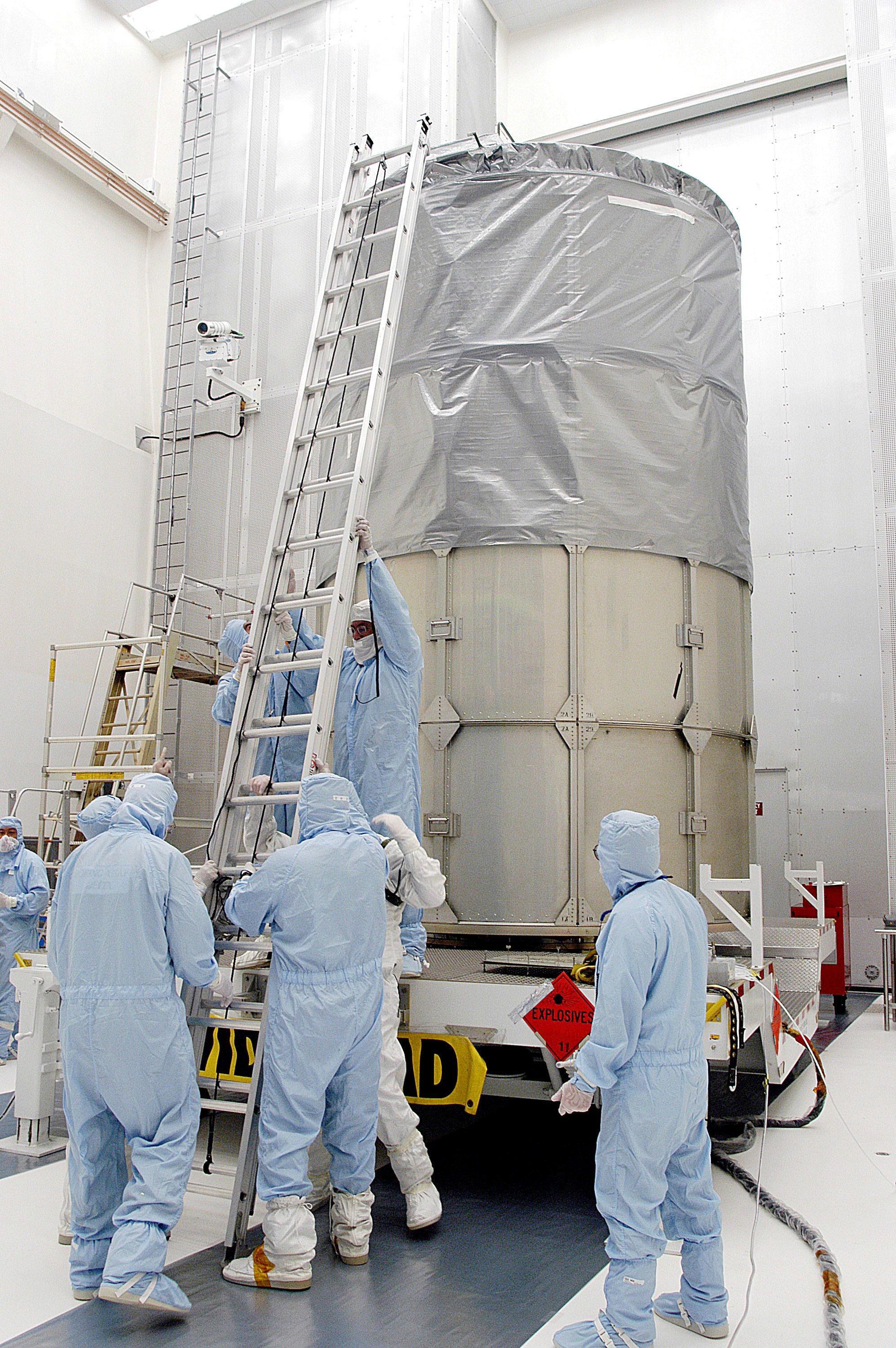KENNEDY SPACE CENTER, FLA. - Workers in NASA Spacecraft Hangar AE erect a ladder to reach the top of the Space Infrared Telescope Facility (SIRTF), which has been returned to the hangar from the launch pad. SIRTF will remain in the clean room until it returns to the pad in early August. One of NASA's largest infrared telescopes to be launched, SIRTF will obtain images and spectra by detecting the infrared energy, or heat, radiated by objects in space.