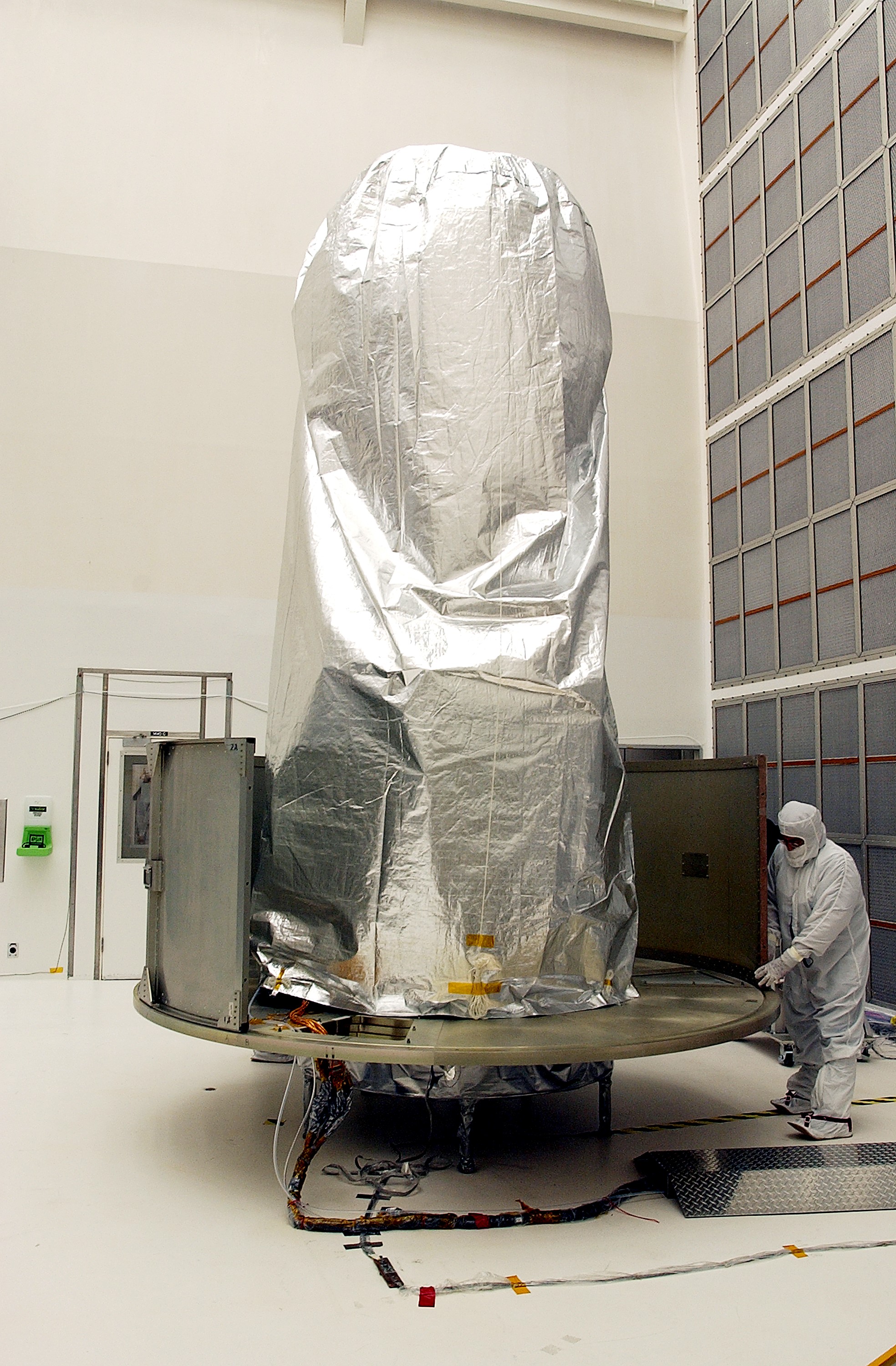 KENNEDY SPACE CENTER, FLA. - A worker at Hangar A&E, Cape Canaveral Air Force Station, place the lower panels of the canister around the Space Infrared Telescope Facility (SIRTF). The spacecraft will be transported to Launch Complex 17-B for mating with its launch vehicle, the Delta II rocket. SIRTF consists of three cryogenically cooled science instruments and an 0.85-meter telescope, and is one of NASA's largest infrared telescopes to be launched. SIRTF will obtain images and spectra by detecting the infrared energy, or heat, radiated by objects in space. Most of this infrared radiation is blocked by the Earth's atmosphere and cannot be observed from the ground.