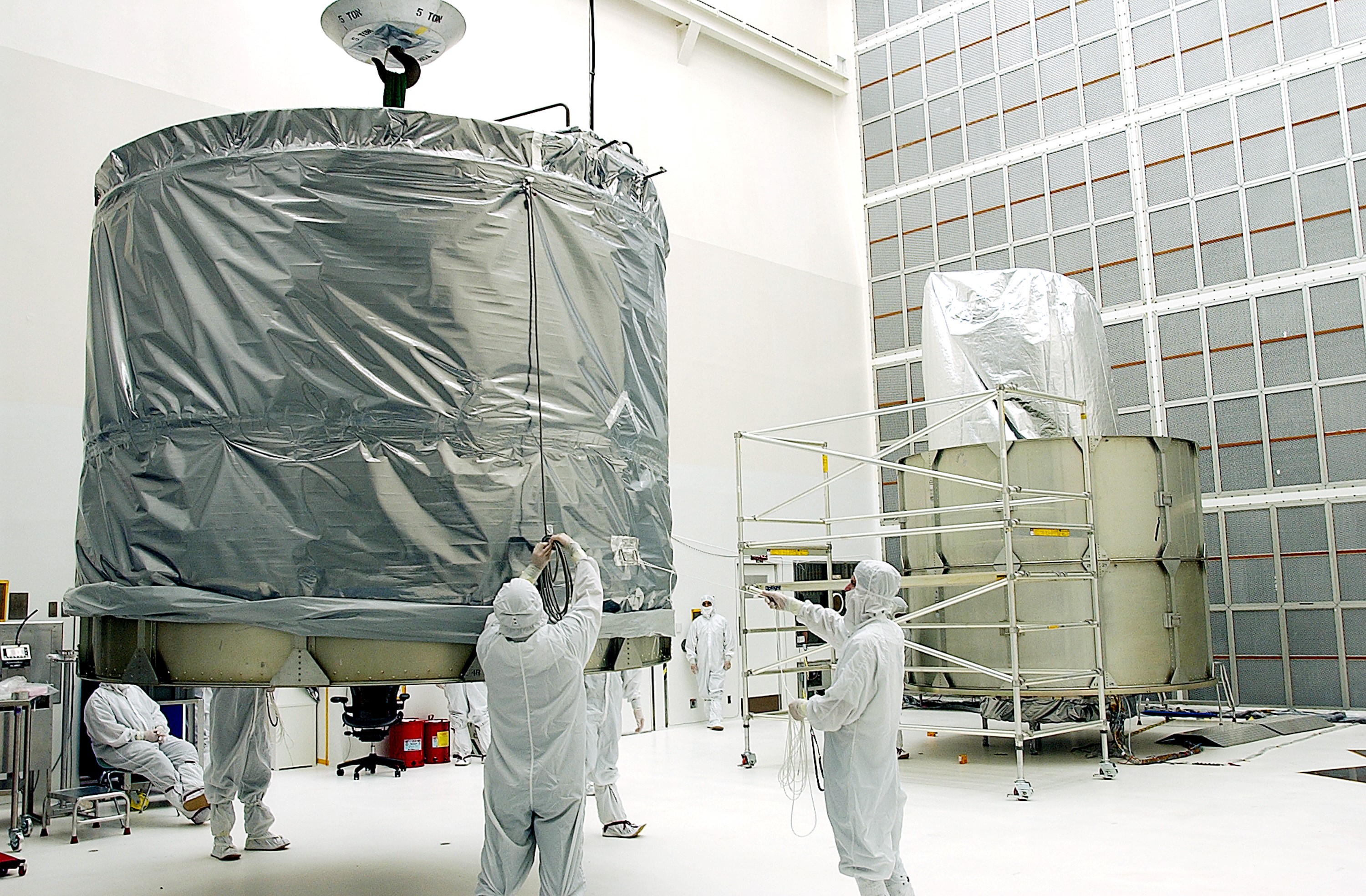 KENNEDY SPACE CENTER, FLA. - Workers at Hangar A&E, Cape Canaveral Air Force Station, lift the upper canister to move it to the Space Infrared Telescope Facility (SIRTF) at right. After encapsulation, the spacecraft will be transported to Launch Complex 17-B for mating with its launch vehicle, the Delta II rocket. SIRTF consists of three cryogenically cooled science instruments and an 0.85-meter telescope, and is one of NASA's largest infrared telescopes to be launched. SIRTF will obtain images and spectra by detecting the infrared energy, or heat, radiated by objects in space. Most of this infrared radiation is blocked by the Earth's atmosphere and cannot be observed from the ground.
