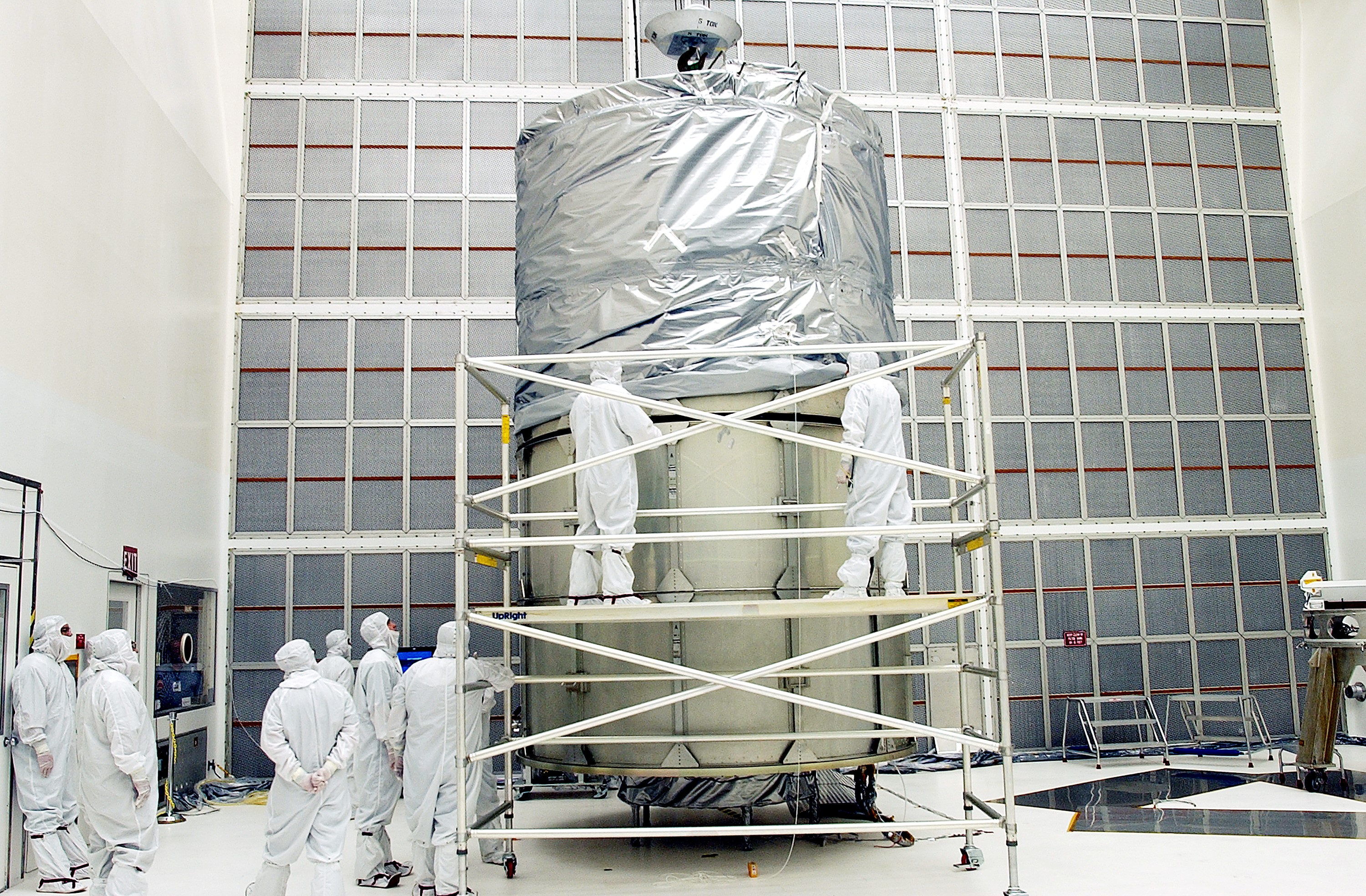 KENNEDY SPACE CENTER, FLA. - Working from a stand, technicians fasten the upper portion of the canister to the middle panels around the Space Infrared Telescope Facility (SIRTF). The spacecraft will be transported to Launch Complex 17-B for mating with its launch vehicle, the Delta II rocket. SIRTF consists of three cryogenically cooled science instruments and an 0.85-meter telescope, and is one of NASA's largest infrared telescopes to be launched. SIRTF will obtain images and spectra by detecting the infrared energy, or heat, radiated by objects in space. Most of this infrared radiation is blocked by the Earth's atmosphere and cannot be observed from the ground.