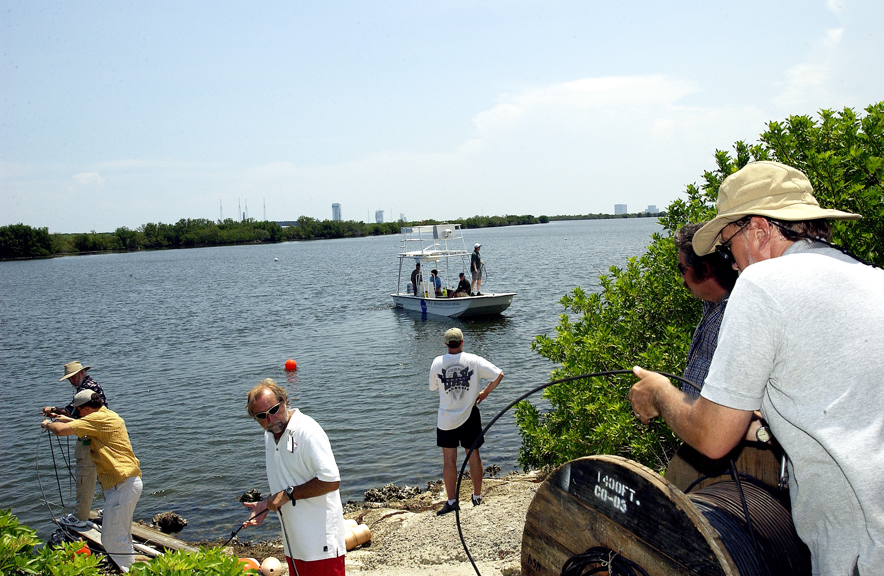 KENNEDY SPACE CENTER, FLA. - Research team members roll out acoustic cable to the water's edge as others stand by in a watercraft during underwater acoustic research being conducted in the Launch Complex 39 turn basin. Several government agencies, including NASA, NOAA, the Navy, the Coast Guard, and the Florida Fish and Wildlife Commission are involved in the testing. The research involves demonstrations of passive and active sensor technologies, with applications in fields ranging from marine biological research to homeland security. The work is also serving as a pilot project to assess the cooperation between the agencies involved. Equipment under development includes a passive acoustic monitor developed by NASA’s Jet Propulsion Laboratory, and mobile robotic sensors from the Navy’s Mobile Diving and Salvage Unit.