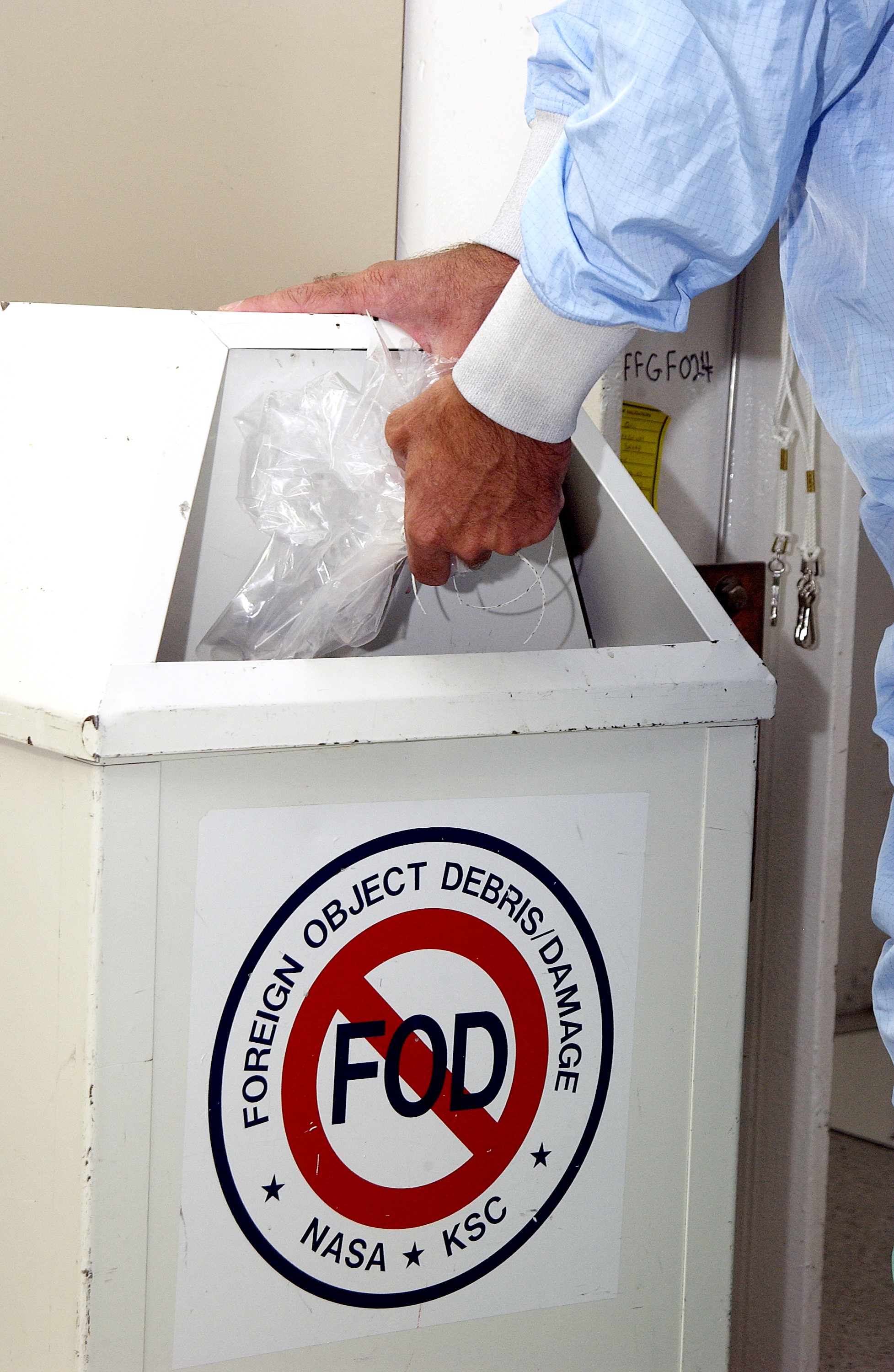 KENNEDY SPACE CENTER, FLA. - A KSC employee dressed in a "bunny suit," standard clean room apparel, disposes of some waste material into a container designated for the purpose. The apparel is designed to cover the hair, clothing and shoes of employees entering a clean room to prevent particulate matter from contaminating the space flight hardware being stored or processed in the room. The suit and container are both part of KSC's Foreign Object Debris (FOD) control program, an important safety initiative.