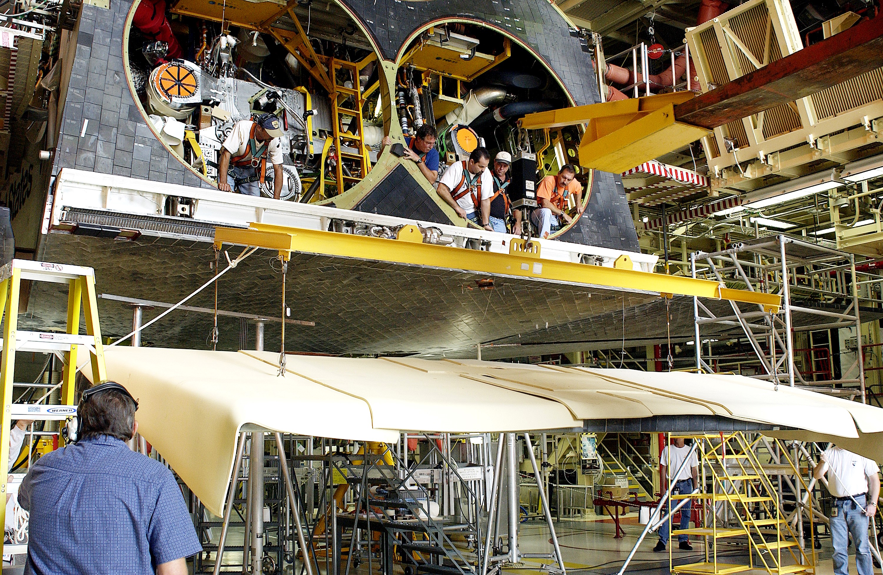 KENNEDY SPACE CENTER, FLA. - In the Orbiter Processing Facility, workers look down from spaces allotted for the main engines as the rear body flap is lifted for installation on the orbiter Discovery. The body flap, which is temporarily under protective covering, attaches below the main engines.
