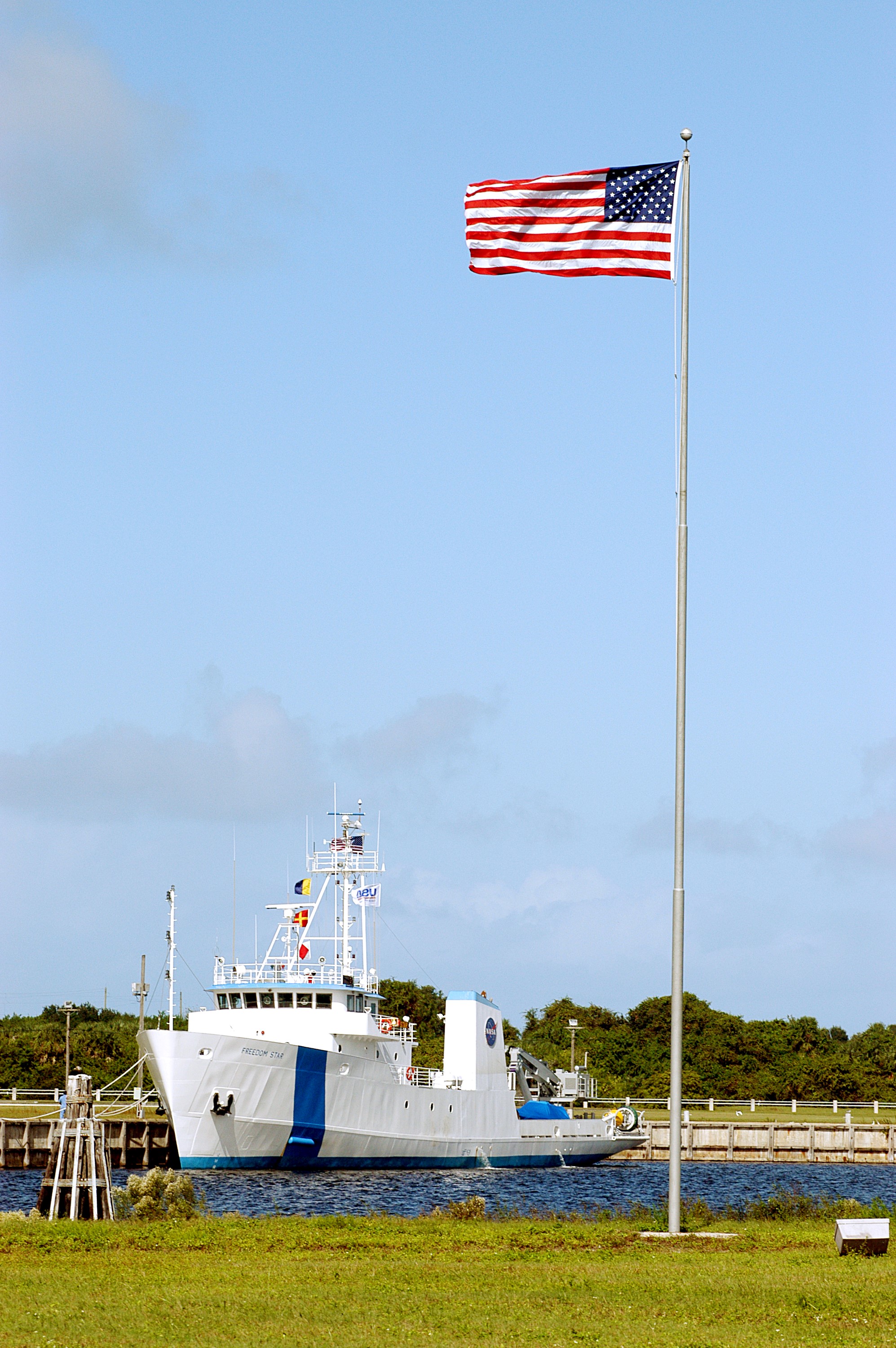 KENNEDY SPACE CENTER, FLA. - The Freedom Star is berthed at the Turn Basin near the Vehicle Assembly Building and NASA-KSC News Center. The flag is near the News Center. The ship has recently returned to KSC after refurbishment at Fort George Island, Fla., including new paint. Freedom Star is one of the solid rocket booster (SRB) retrieval ships built to recover the SRB casings released over the Atlantic Ocean after launch of a Space Shuttle. In addition to the SRBs, the ship recovers the drogue and main parachutes that slow the boosters’ speed before splashdown. The ships also tow the external tanks built at the Michoud Space Systems Assembly Facility near New Orleans to Port Canaveral, Fla. Freedom Star was brought to KSC today for a visit by NATO Parliamentarians.