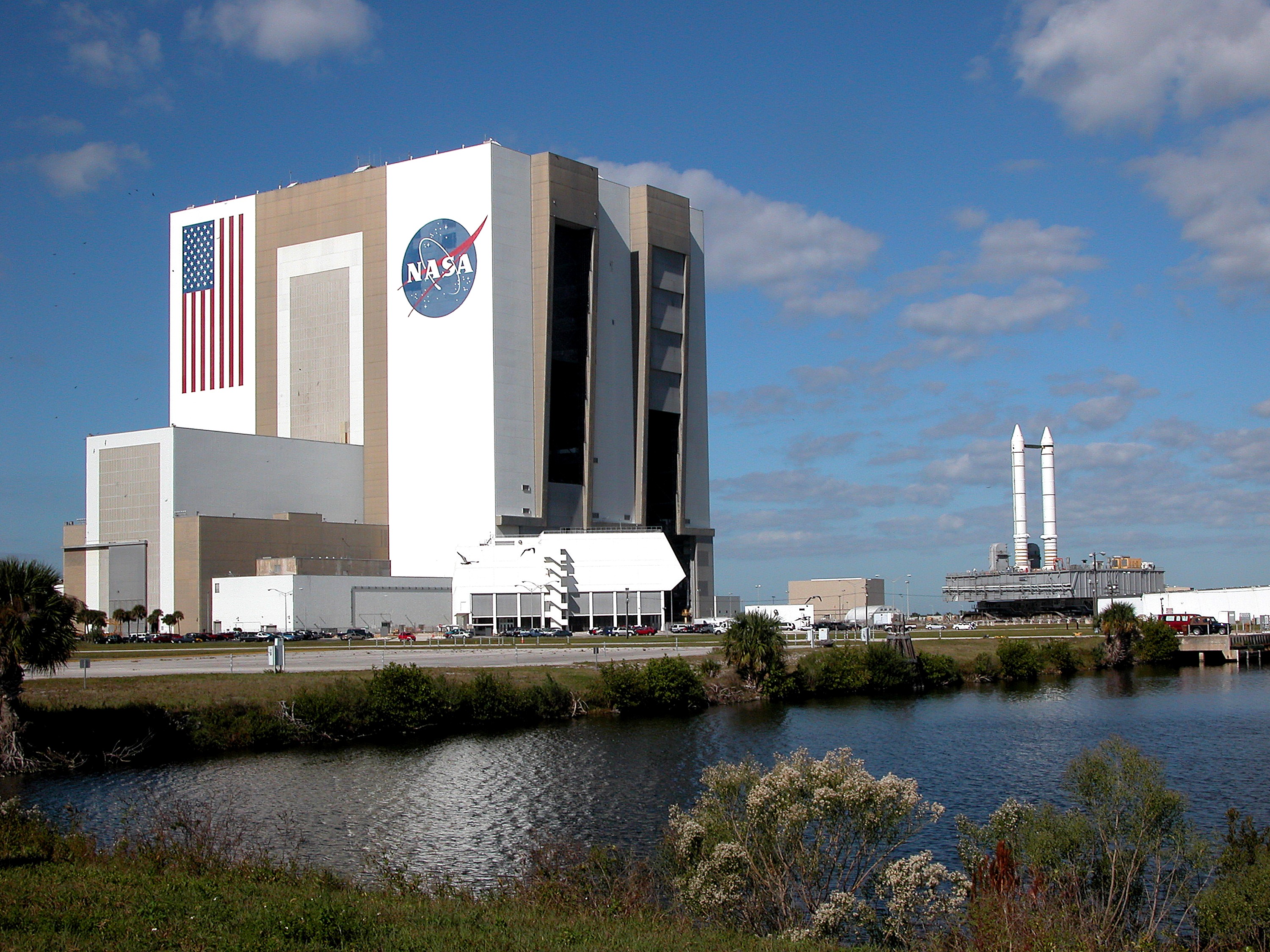 KENNEDY SPACE CENTER, FLA. - Seen across the water of the Launch Complex 39 turn basin, a crawler-transporter, carrying Mobile Launcher Platform (MLP) number 3 with a set of twin solid rocket boosters bolted atop, crawls out of the 525-foot-tall Vehicle Assembly Building during the second engineering analysis vibration test on the crawler and MLP. The crawler is moving at various speeds up to 1 mph in an effort to achieve vibration data gathering goals as it leaves the VAB, travels toward Launch Pad 39A and then returns. The boosters are braced at the top for stability. The primary purpose of these rollout tests is to gather data to develop future maintenance requirements on the transport equipment and the flight hardware. Various parts of the MLP and crawler transporter have been instrumented with vibration data collection equipment.