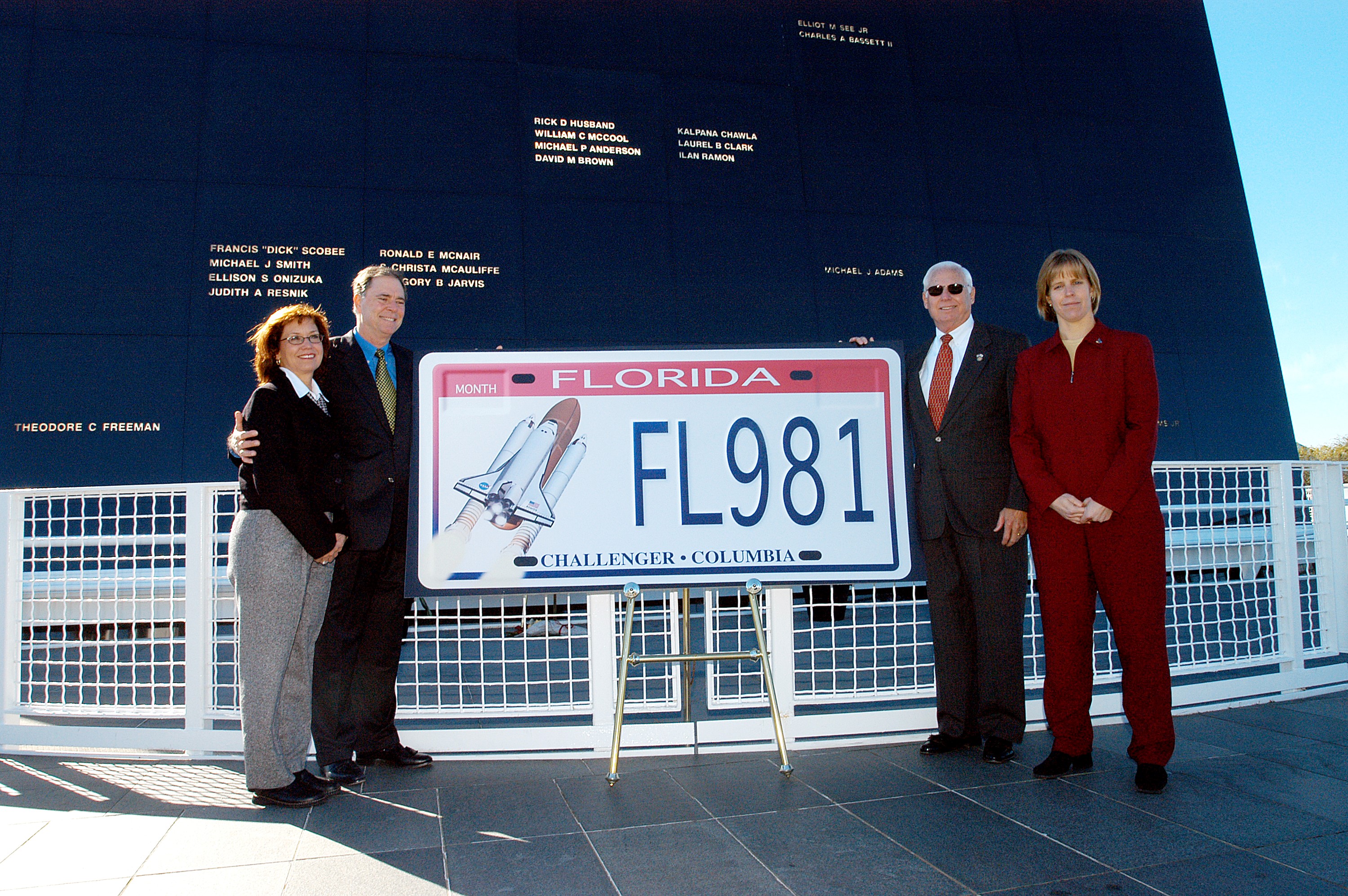 KENNEDY SPACE CENTER, FLA. - The new Florida license plate honoring the fallen astronauts of Challenger and Columbia is unveiled at the KSC Visitor Complex, in front of the Space Memorial Mirror. Participants in the dedication included (from left) Susan Berry, a teacher from Mila Elementary School in Brevard County; Sen. Bill Posey; Florida Rep. Ralph Poppell; and Kirstie McCool Chadwick, sister of William “Willie” J. McCool, who was the pilot on mission STS-107 that ended in disaster Feb. 1, 2003. The Space Mirror, 42-1/2 feet high by 50 feet wide, illuminates the names of the fallen astronauts cut through the monument’s black granite surface.