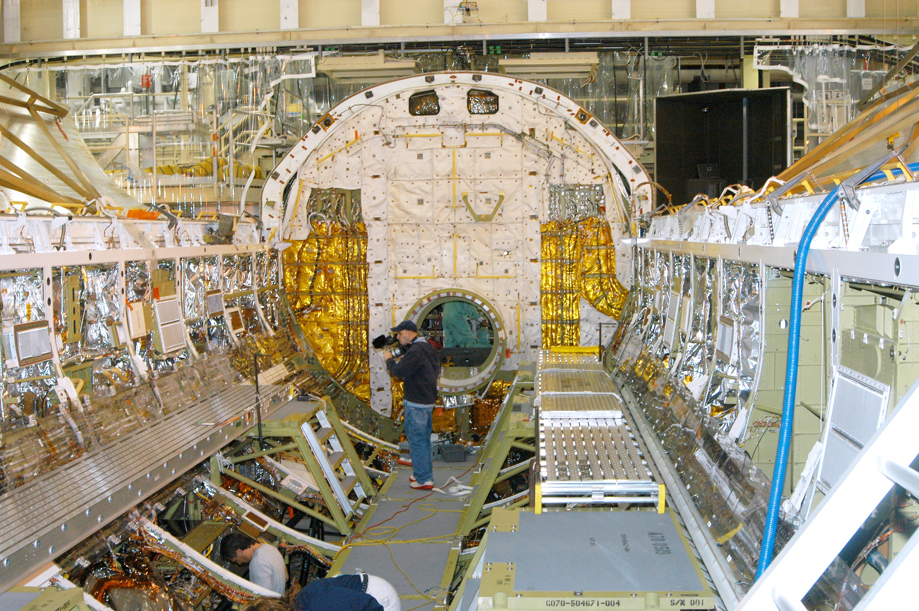 KENNEDY SPACE CENTER, FLA. - In the Orbiter Processing Facility, a cameraman films part of Discovery’s payload bay for a special feature on the KSC Web. In the background is the open hatch of the airlock, located inside the middeck of the spacecraft’s pressurized crew cabin. The airlock is sized to accommodate two fully suited flight crew members simultaneously. Support functions include airlock depressurization and repressurization, extravehicular activity equipment recharge, liquid-cooled garment water cooling, EVA equipment checkout, donning and communications. The outer hatch isolates the airlock from the unpressurized payload bay when closed and permits the EVA crew members to exit from the airlock to the payload bay when open.