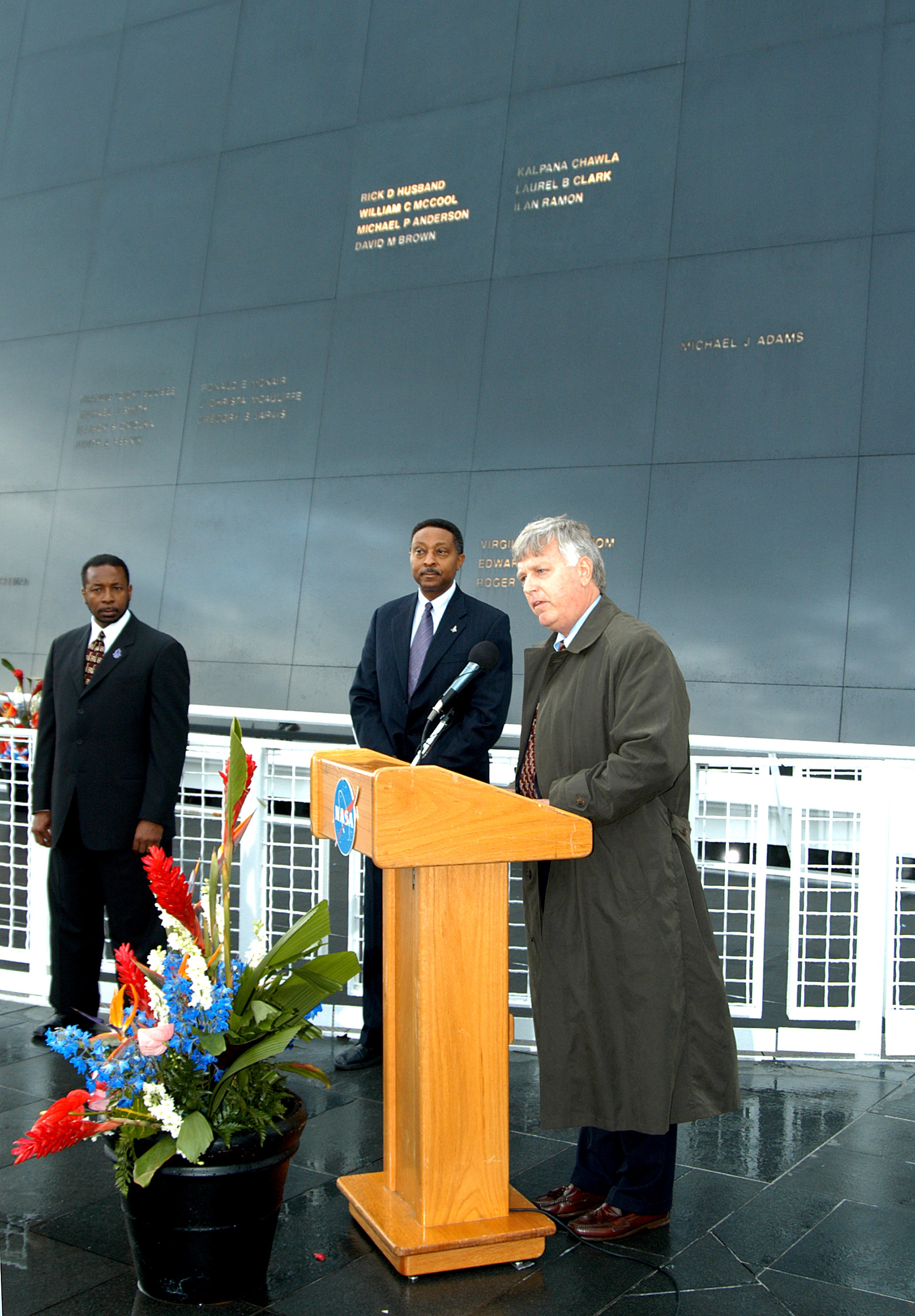 KENNEDY SPACE CENTER, FLA. - Center Director Jim Kennedy (right) speaks to attendees at a memorial service honoring the crew of Columbia. At left are KSC Deputy Director Woodrow Whitlow Jr. and Executive Director of Florida Space Authority Winston Scott, who was an invited speaker. Scott is a former astronaut who flew on Columbia in 1997. They are standing in front of the Space Memorial Mirror at the KSC Visitor Complex. Feb. 1 is the one-year anniversary of the loss of the crew and orbiter Columbia in a tragic accident as the ship returned to Earth following mission STS-107. Attended by many friends, co-workers and families, the memorial service was also open to the public.