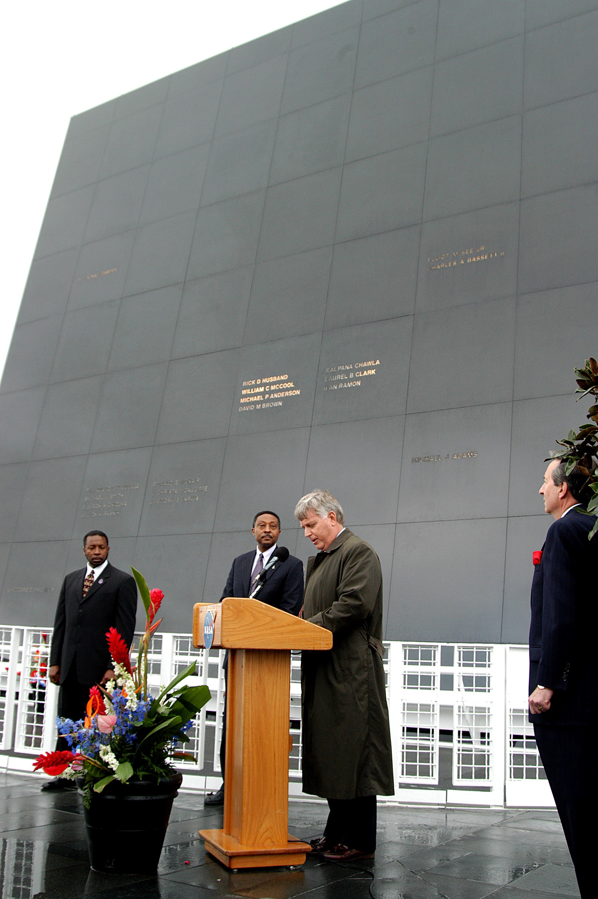 KENNEDY SPACE CENTER, FLA. - In front of the Space Memorial Mirror at the KSC Visitor Complex, Center Director Jim Kennedy (right) speaks to visitors gathered for the memorial service honoring the crew of Columbia. At left are KSC Deputy Director Woodrow Whitlow Jr. and Executive Director of Florida Space Authority Winston Scott; at right is Dr. Stephen Feldman, president of the Astronaut Memorial Foundation. Feb. 1 is the one-year anniversary of the loss of the crew and orbiter Columbia in a tragic accident as the ship returned to Earth following mission STS-107. The public was also invited to the memorial service held at the KSC Visitor Complex.