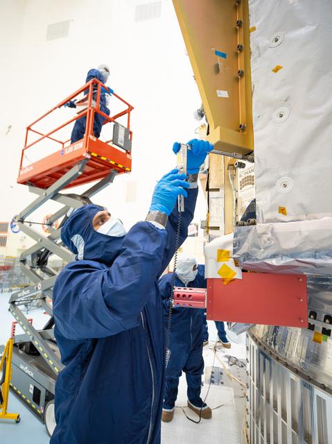 People in blue protective suits and a red cherry picker work in an industrial high bay.