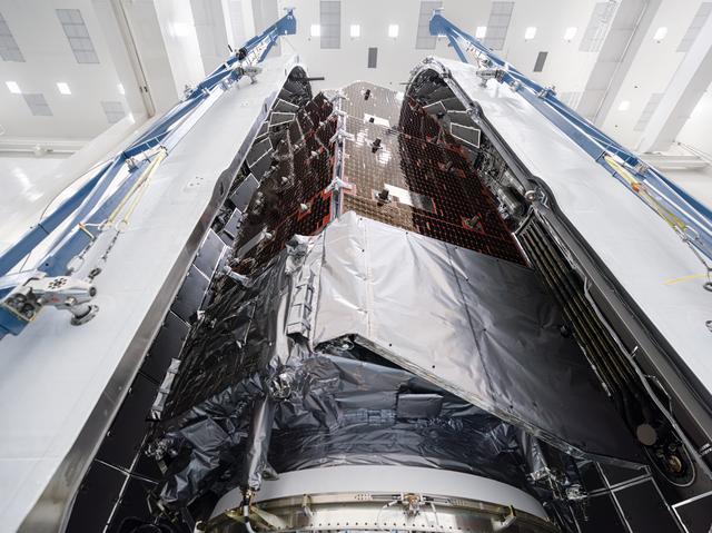 Wide-angle interior view of the payload fairing with NASA’s Roman Space Telescope secured inside. The telescope is wrapped in protective material, and tall blue support structures rise along both sides.