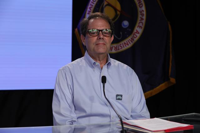 A panelist sits behind a long, illuminated desk in front a video wall featuring NASA's Nancy Grace Roman Space Telescope during a NASA news conference. 