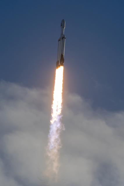 A rocket lifts off from a coastal launch pad, sending bright flames and a plume of white smoke across the ground.