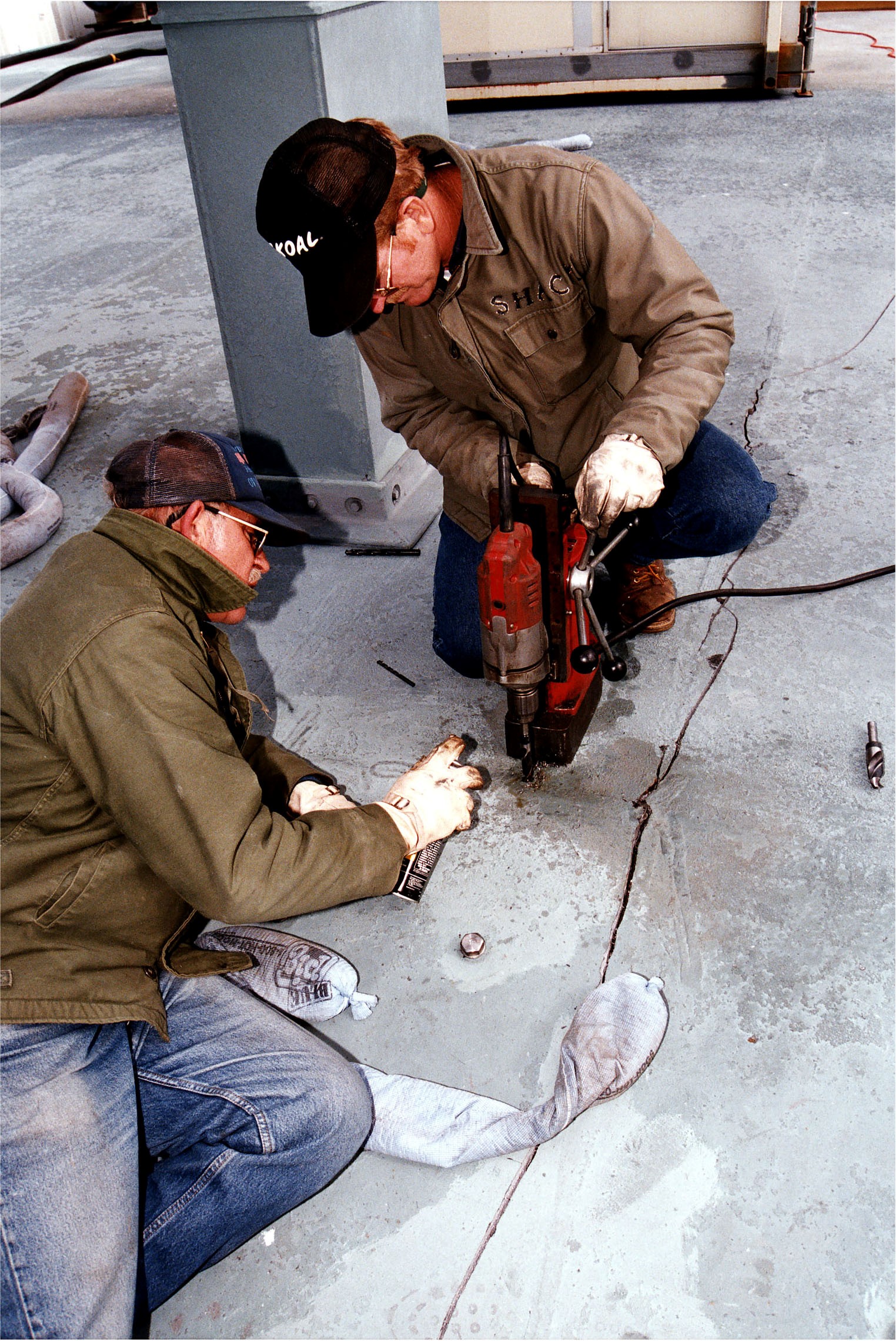 KENNEDY SPACE CENTER, FLA. - United Space Alliance (USA) workers J.D. Wise, left, and Robert Shackelford, with drill, try to stop an approximately 24-foot-long crack from getting any bigger on the Mobile Launcher Platform (MLP), which is holding the Space Shuttle Discovery en route to Launch Pad 39A for the STS-82 mission. Discovery was on its way out to the launch pad when engineers heard a loud bang and noticed that a crack had developed on the MLP. Rollout had begun shortly after 7 a.m. EST and was stopped at about 8:25 a.m. This Y-shaped crack is on the MLP surface and runs from near the left-hand solid rocket booster flame hole toward the near corner of the MLP. Rollout of Discovery resumed just past noon after structural engineers determined that the integrity of the MLP had not been compromised. Discovery is scheduled to lift off on the second Hubble Space Telescope servicing mission on Feb. 11.