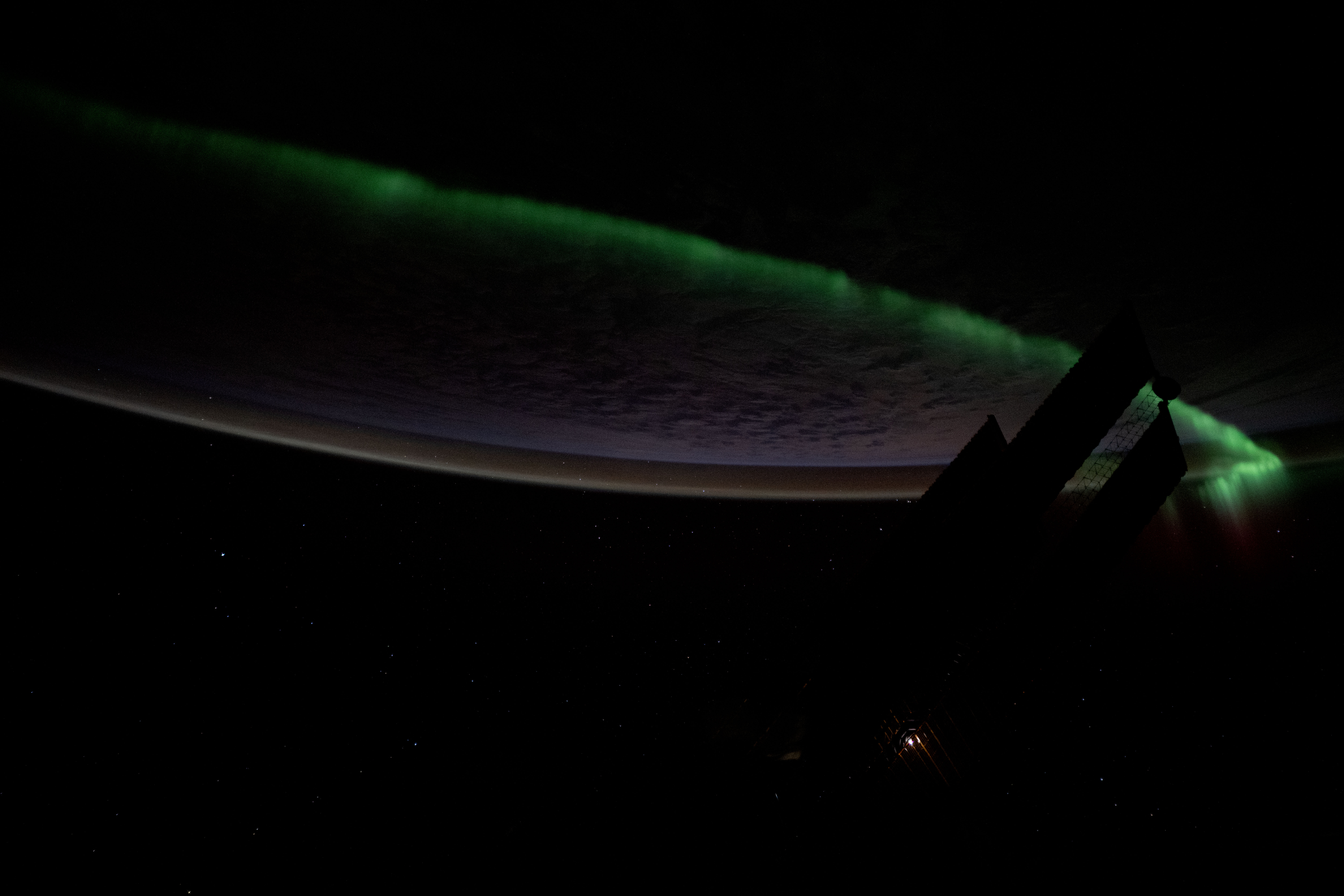 An atmospheric glow crowns Earth's horizon as an aurora streams
