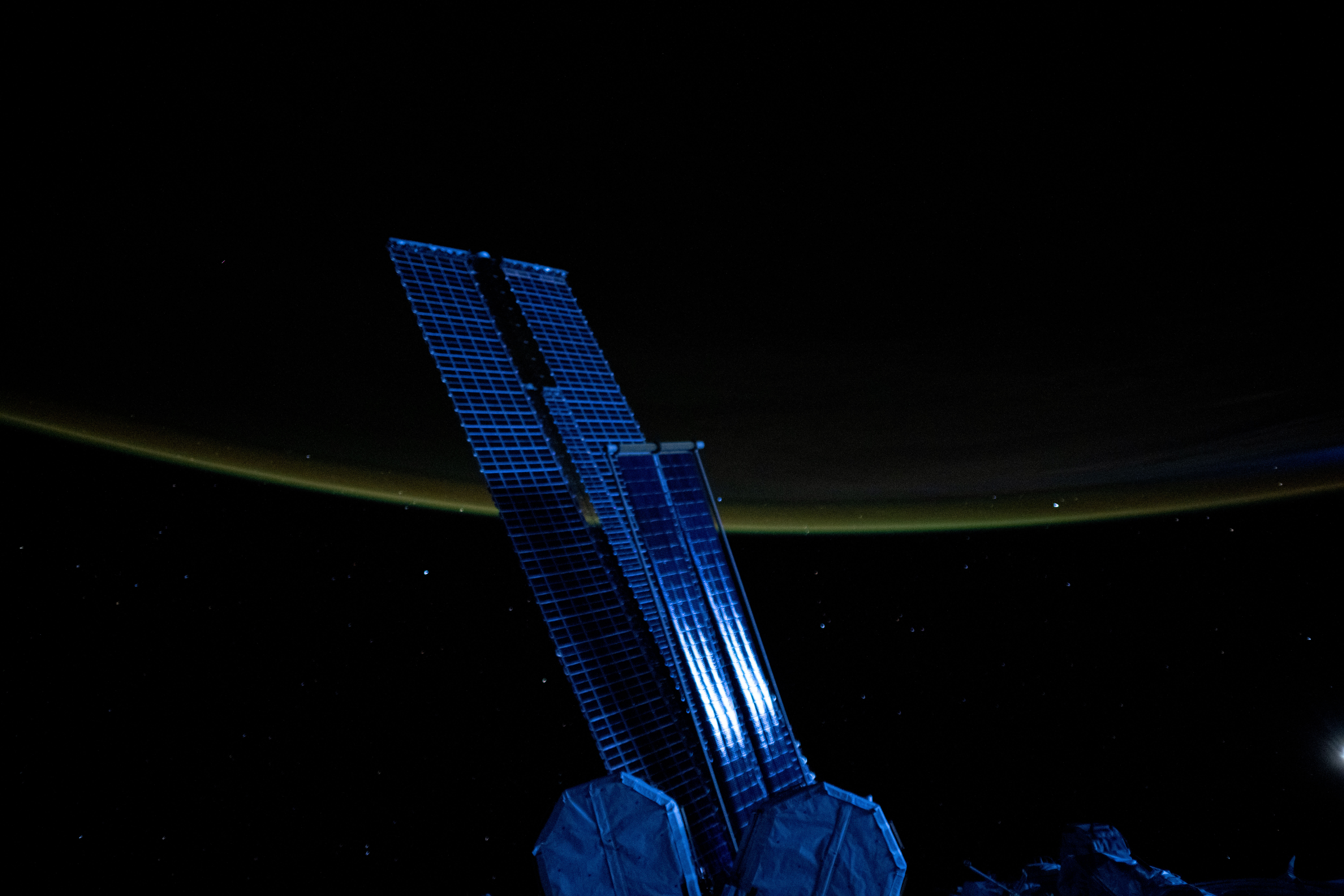 Moonlight casts a blue light on a set of the space station's main solar arrays and rollout solar arrays