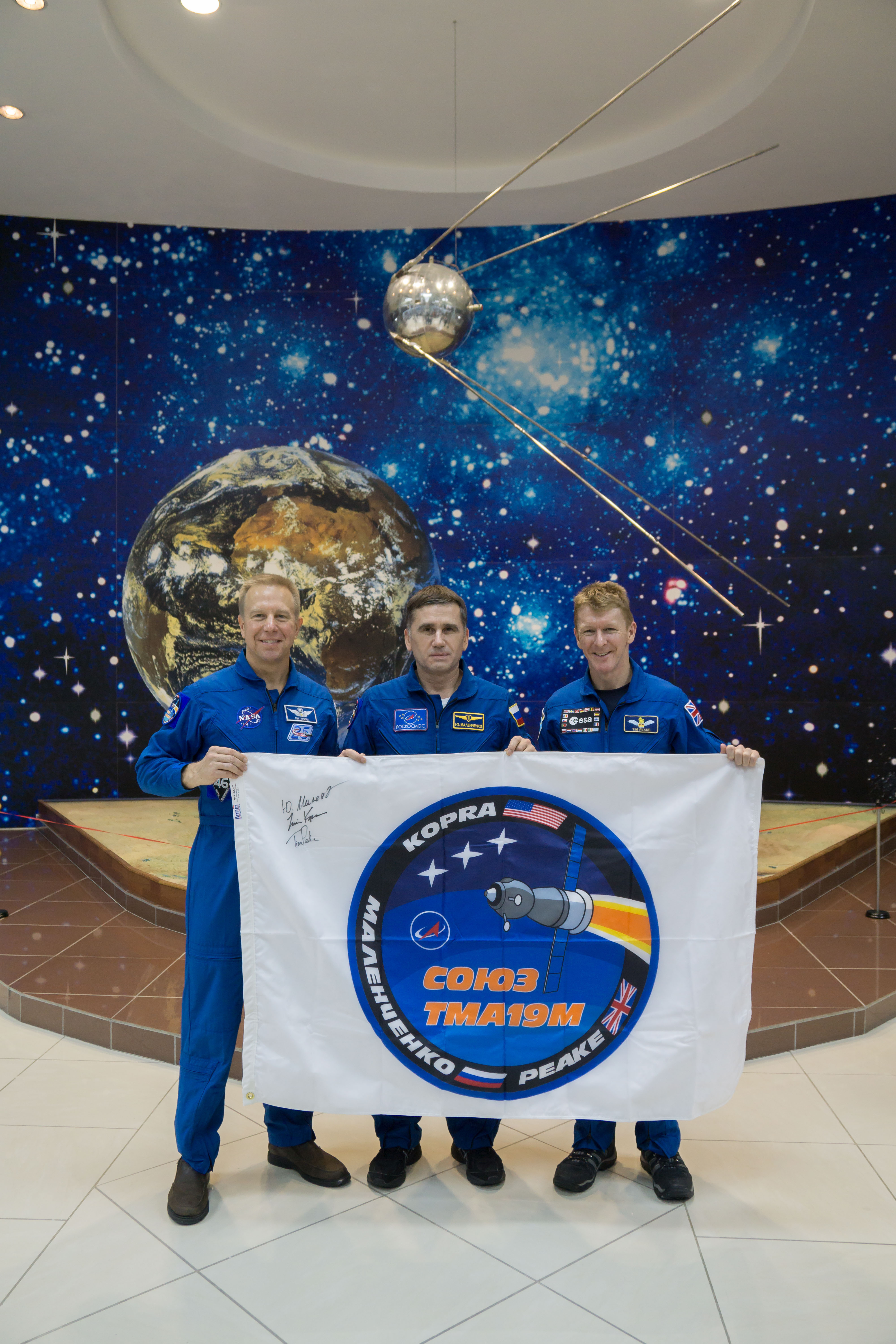 During a break from training, the Expedition 46-47 crewmembers toured the Korolev Museum at the Baikonur Cosmodrome in Kazakhstan Dec. 10 and displayed a flag bearing the logo for their Soyuz mission. From left to right are Tim Kopra of NASA, Yuri Malenchenko of the Russian Federal Space Agency (Roscosmos) and Tim Peake of the European Space Agency. Kopra, Peake and Malenchenko will launch Dec. 15 on the Soyuz TMA-19M spacecraft for a six-month mission on the International Space Station...NASA/Victor Zelentsov.