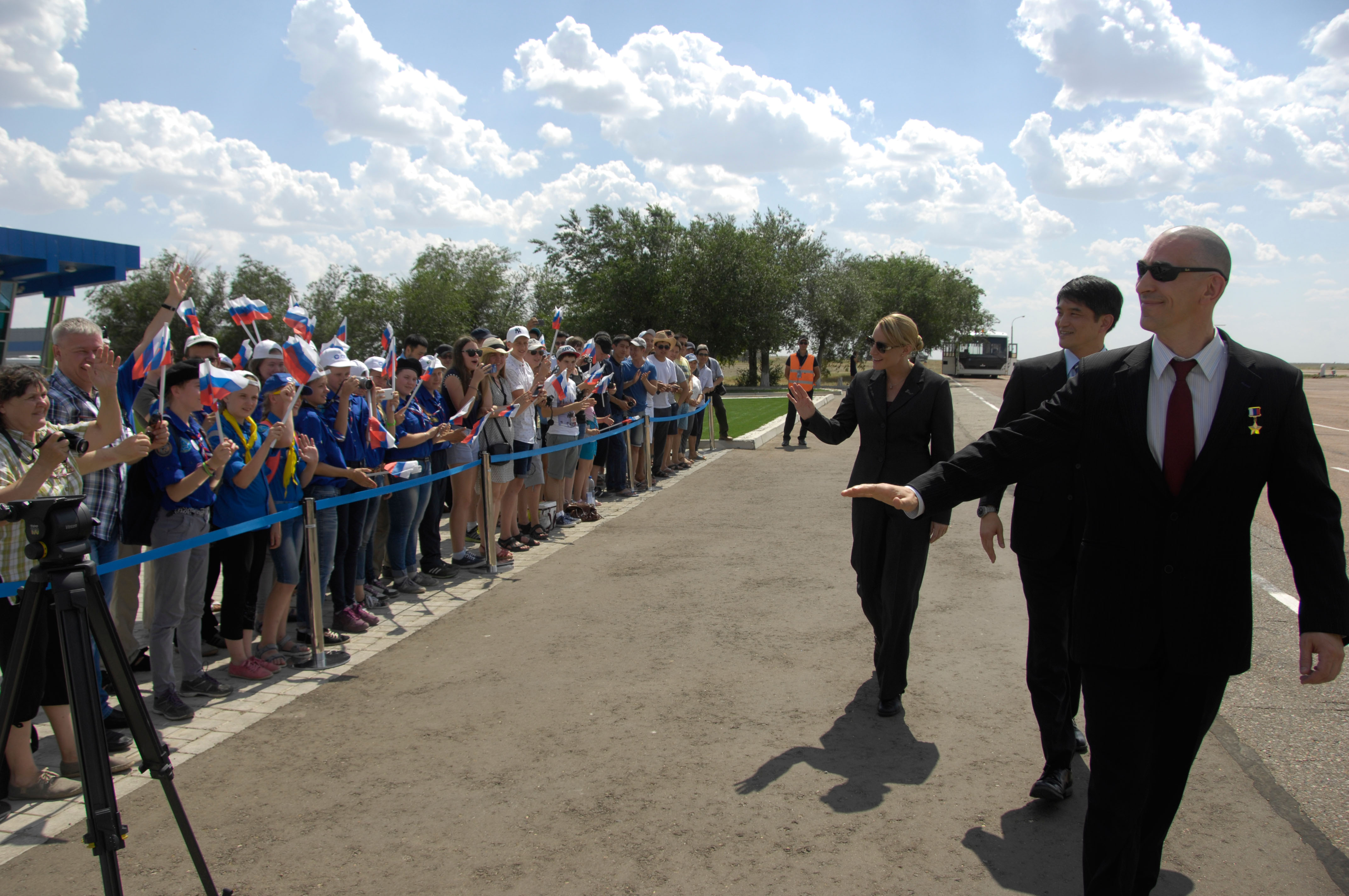 ISS Expedition 48-49 prime crewmembers Kate Rubins of NASA (left), Takuya Onishi of the Japan Aerospace Exploration Agency (center) and Anatoly Ivanishin of Roscosmos (right) wave to schoolchildren after arriving in Baikonur, Kazakhstan June 24 for final pre-launch training following a flight from Star City, Russia. The trio will launch July 7 from the Baikonur Cosmodrome in Kazakhstan on the Soyuz MS-01 spacecraft for a planned four-month mission on the International Space Station...NASA/Alexander Vysotsky.