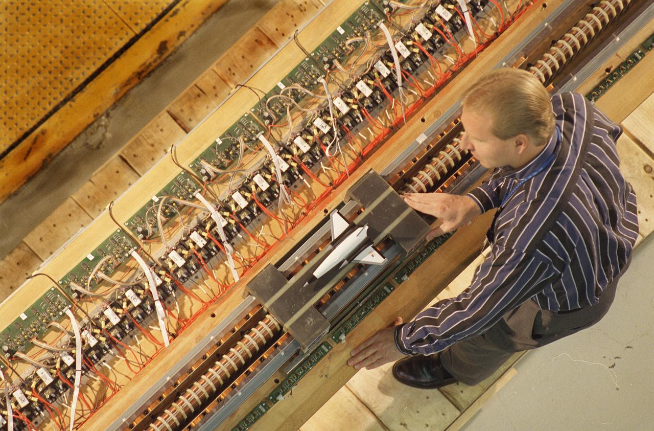 Marshall Space Flight Center’s (MSFC’s) Advanced Space Transportation Program has developed the Magnetic Launch Assist System, formerly known as the Magnetic Levitation (MagLev) technology that could give a space vehicle a running start to break free from Earth’s gravity.  A Magnetic Launch Assist system would use magnetic fields to levitate and accelerate a vehicle along a track at speeds up to 600 mph.  The vehicle would shift to rocket engines for launch into orbit.  Similar to high-speed trains and roller coasters that use high-strength magnets to lift and propel a vehicle a couple of inches above a guideway, a Magnetic Launch Assist system would electromagnetically propel a space vehicle along the track. The tabletop experimental track for the system shown in this photograph is 44-feet long, with 22-feet of powered acceleration and 22-feet of passive braking. A 10-pound carrier with permanent magnets on its sides swiftly glides by copper coils, producing a levitation force. The track uses a linear synchronous motor, which means the track is synchronized to turn the coils on just before the carrier comes in contact with them, and off once the carrier passes. Sensors are positioned on the side of the track to determine the carrier’s position so the appropriate drive coils can be energized. MSFC engineers have conducted tests on the indoor track and a 50-foot outdoor track. The major advantages of launch assist for NASA launch vehicles is that it reduces the weight of the take-off, the landing gear, the wing size, and less propellant resulting in significant cost savings. The US Navy and the British MOD (Ministry of Defense) are planning to use magnetic launch assist for their next generation aircraft carriers as the aircraft launch system.  The US Army is considering using this technology for launching target drones for anti-aircraft training. 