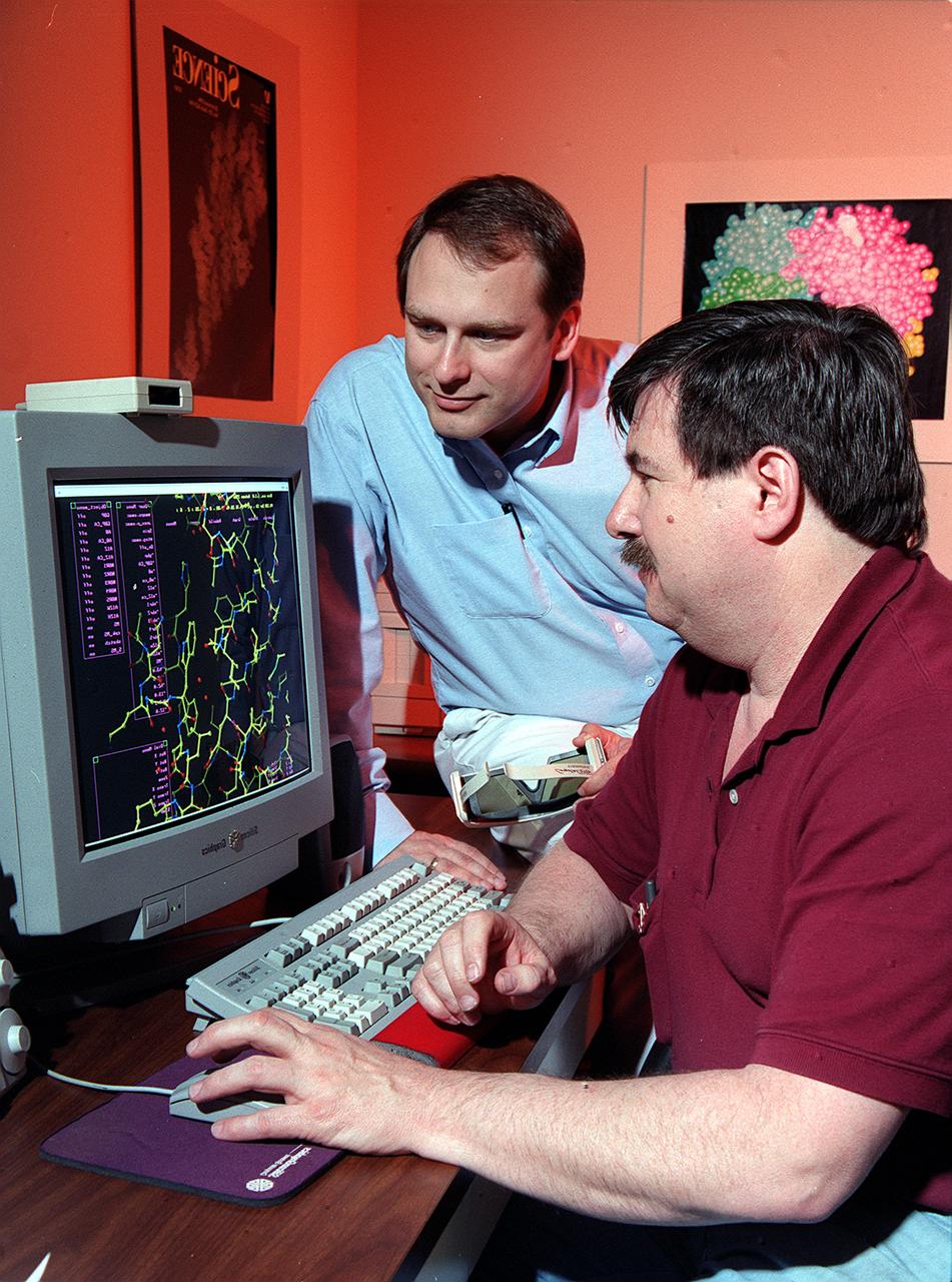 Dr. Marc Pusey (seated) and Dr. Craig Kundrot use computers to analyze x-ray maps and generate three-dimensional models of protein structures. With this information, scientists at Marshall Space Flight Center can learn how proteins are made and how they work. The computer screen depicts a proten structure as a ball-and-stick model. Other models depict the actual volume occupied by the atoms, or the ribbon-like structures that are crucial to a protein's function. 