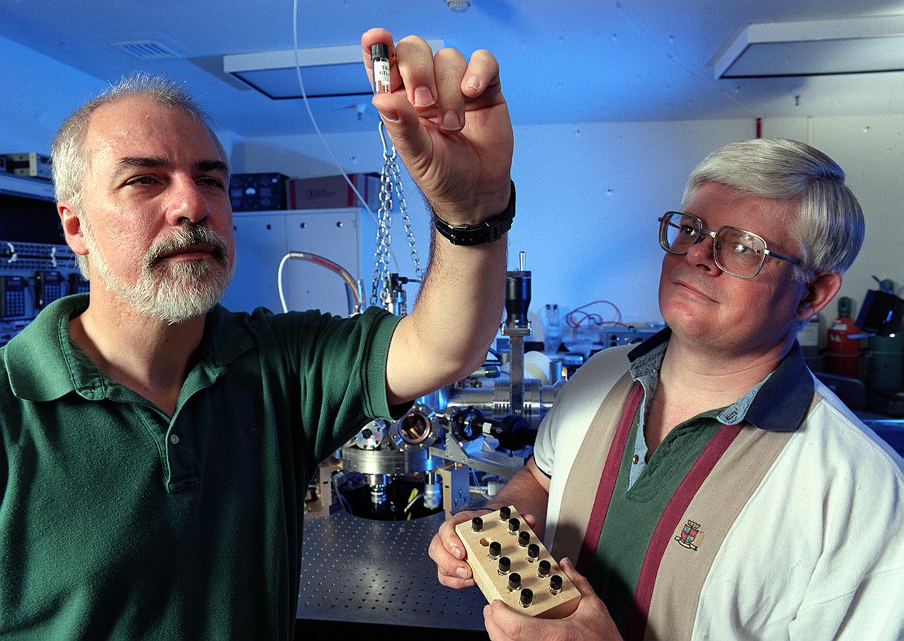 Prof. Kerneth Kelton of Washington University in St. Lous, MO, (L) and Dr. Michael Robinson of NASA's Marshall Space Flight Center (MSFC) examine a titanium-iron silicate (TiFeSiO)sample processed in MSFC's Electrostatic Levitator (ESL) Facility (background). Kelton is investigating undercooling of polytetrahedral phase-forming liquids.