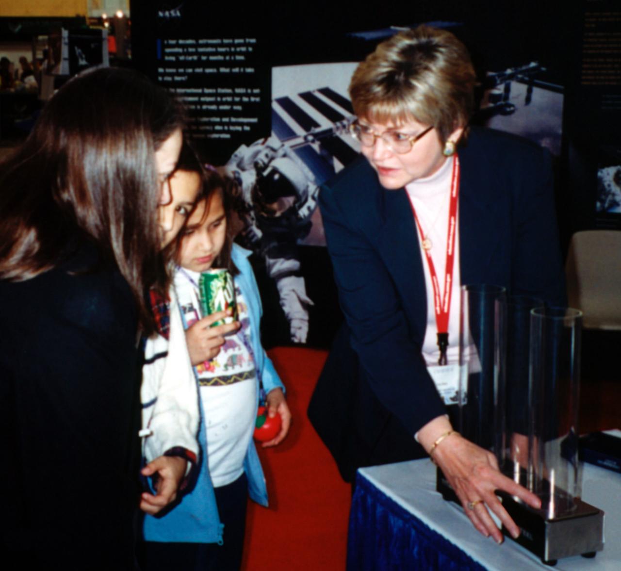 Pat Doty (right) of NASA/Marshall Space Flight Center (MSFC) demonstrates the greater bounce to the ounce of metal made from a supercooled bulk metallic glass alloy that NASA is studying in space experiments. The metal plates at the bottom of the plexiglass tubes are made of three different types of metal. Bulk metallic glass is more resilient and, as a result, the dropped ball bearing bounces higher. Experiments in space allow scientists to study fundamental properties that carnot be observed on Earth. This demonstration was at the April 2000 conference of the National Council of Teachers of Mathematics in Chicago. Photo credit: NASA/Marshall Space Flight Center (MSFC)