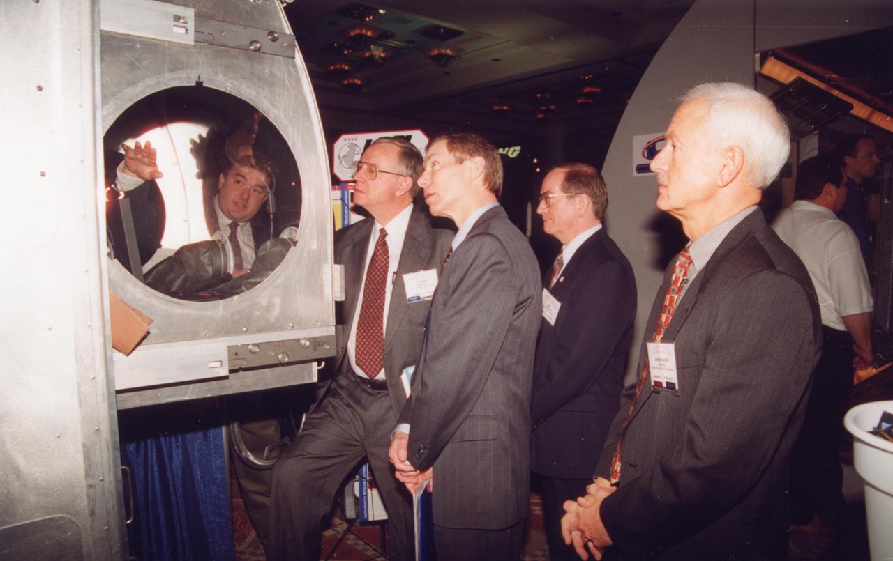 Tim Broach (seen through window) of NASA/Marshall Spce Flight Center (MSFC), demonstrates the working volume inside the Microgravity Sciences Glovebox being developed by the European Space Agency (ESA) for use aboard the U.S. Destiny laboratory module on the International Space Station (ISS). This mockup is the same size as the flight hardware. Observing are Tommy Holloway and Brewster Shaw of The Boeing Co. (center) and John-David Bartoe, ISS research manager at NASA/John Space Center and a payload specialist on Spacelab-2 mission (1985). Photo crdit: NASA/Marshall Space Flight Center (MSFC)