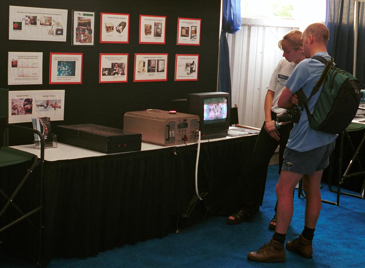 Two visitors watch a TV monitor showing plant growth inside a growth chamber designed for operation aboard the Space Shuttle as part of NASA's Space Product Development program. The exhibit, featuring work by the Wisconsin Center for Space Automation and Robotics, was at AirVenture 2000 sponsored by the Experimental Aircraft Association in Oshkosh, WI.
