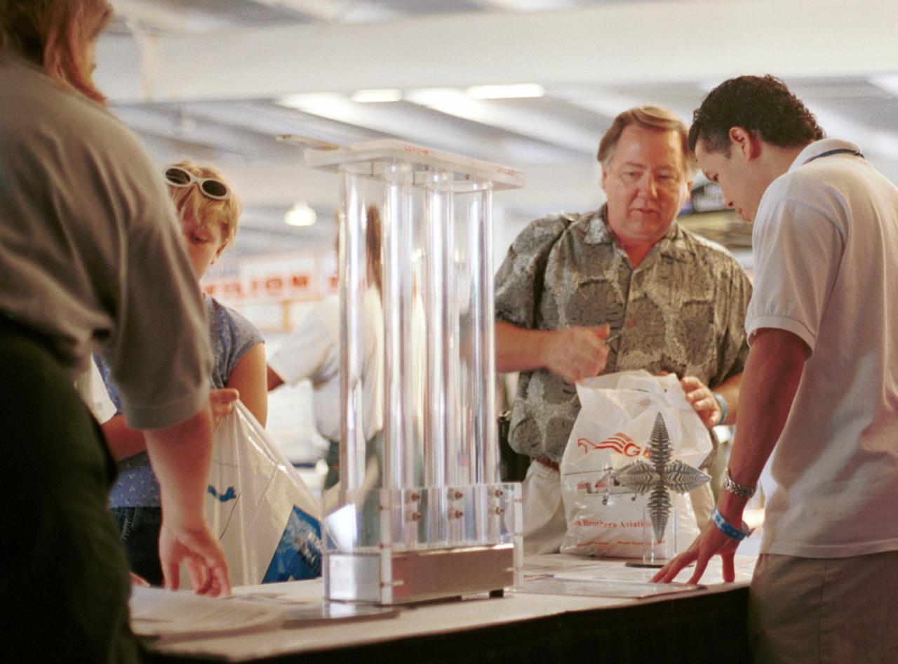 Paul Luz (right), an aerospace flight systems engineer at NASA's Marshall Space Flight Center (MSFC), takes a question from a visitor as they discuss microgravity research at AirVenture 2000. Part of the NASA exhibits included demonstrations of knowledge gained from microgravity research aboard the Space Shuttle. These include liquid metal (liquid metal demonstrator is three plastic drop tubes at center) and dendritic growth (in front of Luz), both leading to improvements in processes of Earth. The exhibit was part of the NASA outreach activity at AirVenture 2000 sponsored by the Experimental Aircraft Association in Oshkosh, WI. 