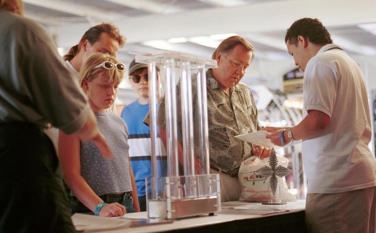 Paul Luz (right), an aerospace flight system engineer at NASA's Marshall Space Flight Center (MSFC), discusses microgravity research with a visitor at AirVenture 2000. Part of the NASA exhibits included demonstration of knowledge gained from micorgravity research aboard the Space Shuttle. These include liquid metal (Liquid metal demonstrator is three plastic drop tubes at center) and dendritic growth (in front of Luz), both leading to improvements in processes on Earth. The exhibit was part of the NASA outreach activity at AirVenture 2000 sponsored by the Experimental Aircraft Association in Oshkosh, WI. 