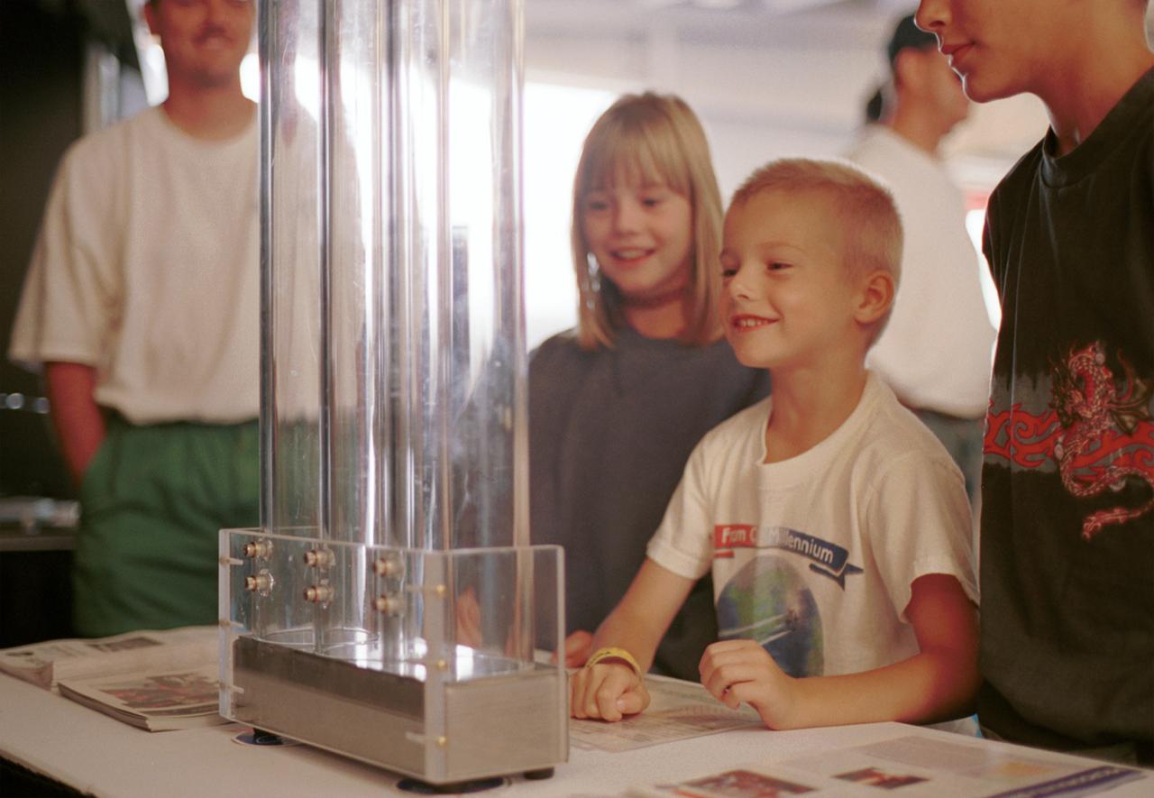 An entranced youngster watches a demonstration of the enhanced resilience of undercooled metal alloys as compared to conventional alloys. Steel bearings are dropped onto plates made of steel, titanium alloy, and zirconium liquid metal alloy, so-called because its molecular structure is amorphous and not crystalline. The bearing on the liquid metal plate bounces for a minute or more longer than on the other plates. Experiments aboard the Space Shuttle helped scientists refine their understanding of the physical properties of certain metal alloys when undercooled (i.e., kept liquid below their normal solidification temperature). This new knowledge then allowed scientists to modify a terrestrial production method so they can now make limited quantities marketed under the Liquid Metal trademark. The exhibit was a part of the NASA outreach activity at AirVenture 2000 sponsored by the Experimental Aircraft Association in Oshkosh, WI.