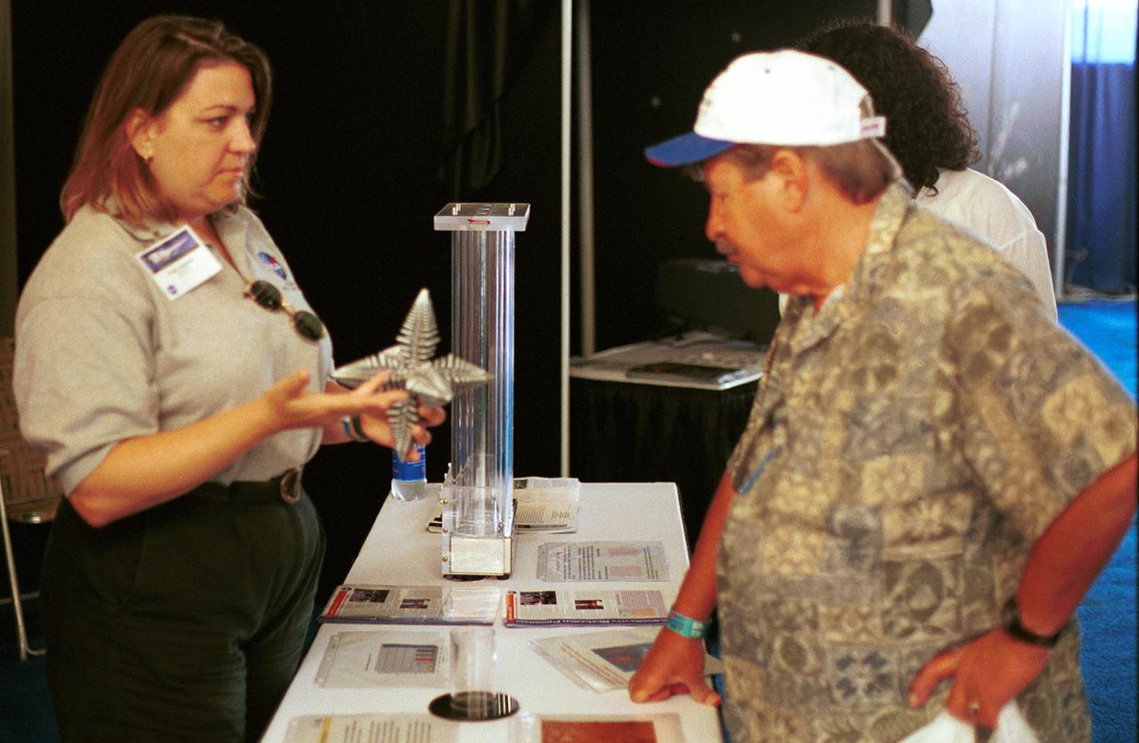 Angie Jackman, a NASA project manager in microgravity research, explains a model of a dendrite to a visitor to the NASA exhibit at AirVenture 2000 sponsored by the Experimental Aircraft Association in Oshkosh, WI. The model depicts microscopic dendrites that grow as molten metals solidify. NASA sponsored three experiments aboard the Space Shuttle that used the microgravity environment to study the formation of large (1 to 4 mm) dendrites without Earth's gravity disrupting their growth. Three advanced follow-on experiments, managed by Jackman, are being developed for the International Space Station (ISS). 