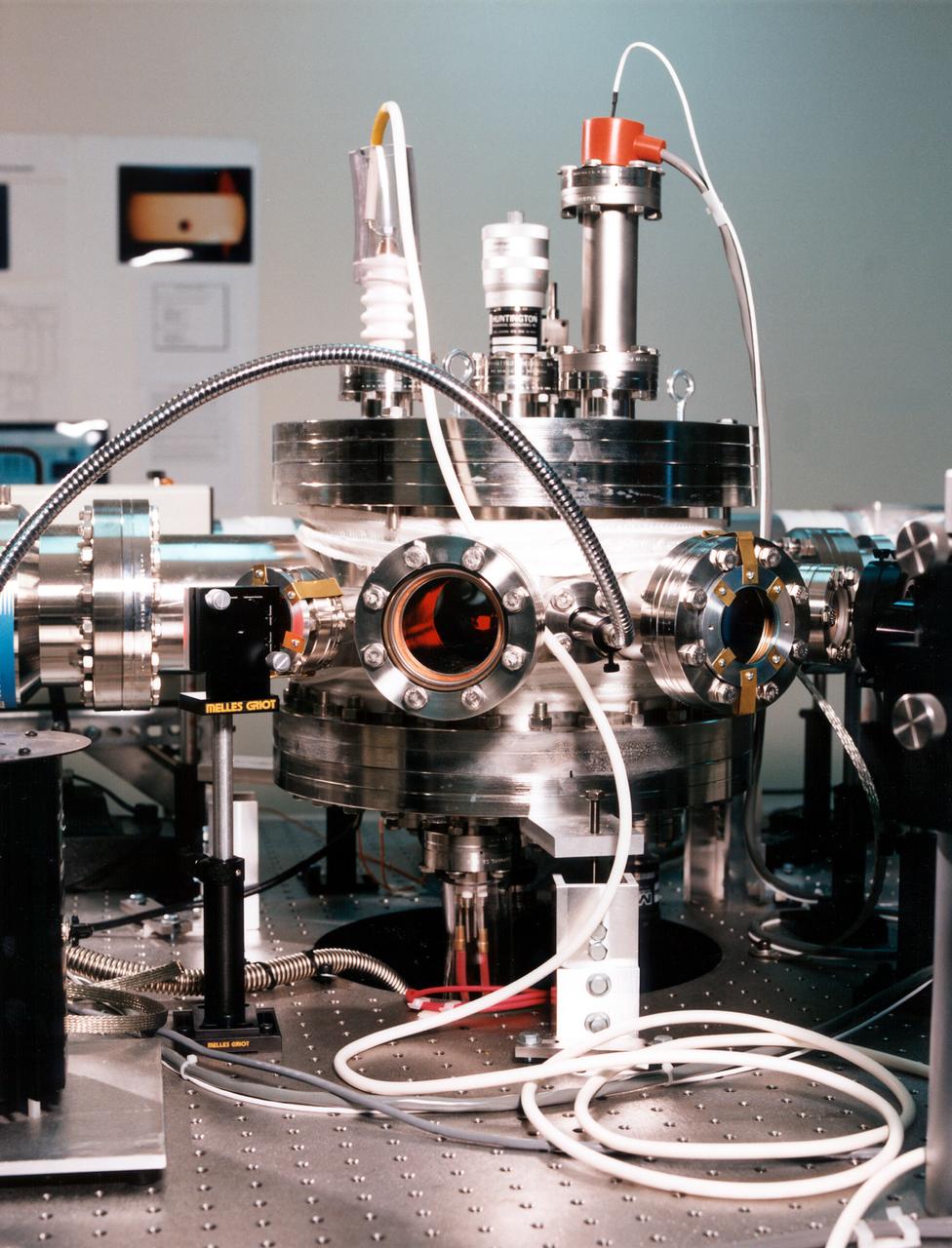 Optical prots ring the Electrostatic Levitator (ESL) vacuum chamber to admit light from the heating laser (the beam passes through the window at left), poisitioning lasers (one port is at center), and lamps (arc lamp at right), and to allow diagnostic instruments to view the sample. The ESL uses static electricity to suspend an object (about 2-3 mm in diameter) inside a vacuum chamber while a laser heats the sample until it melts. This lets scientists record a wide range of physical properties without the sample contacting the container or any instruments, conditions that would alter the readings. The Electrostatic Levitator is one of several tools used in NASA's microgravity materials science program. 