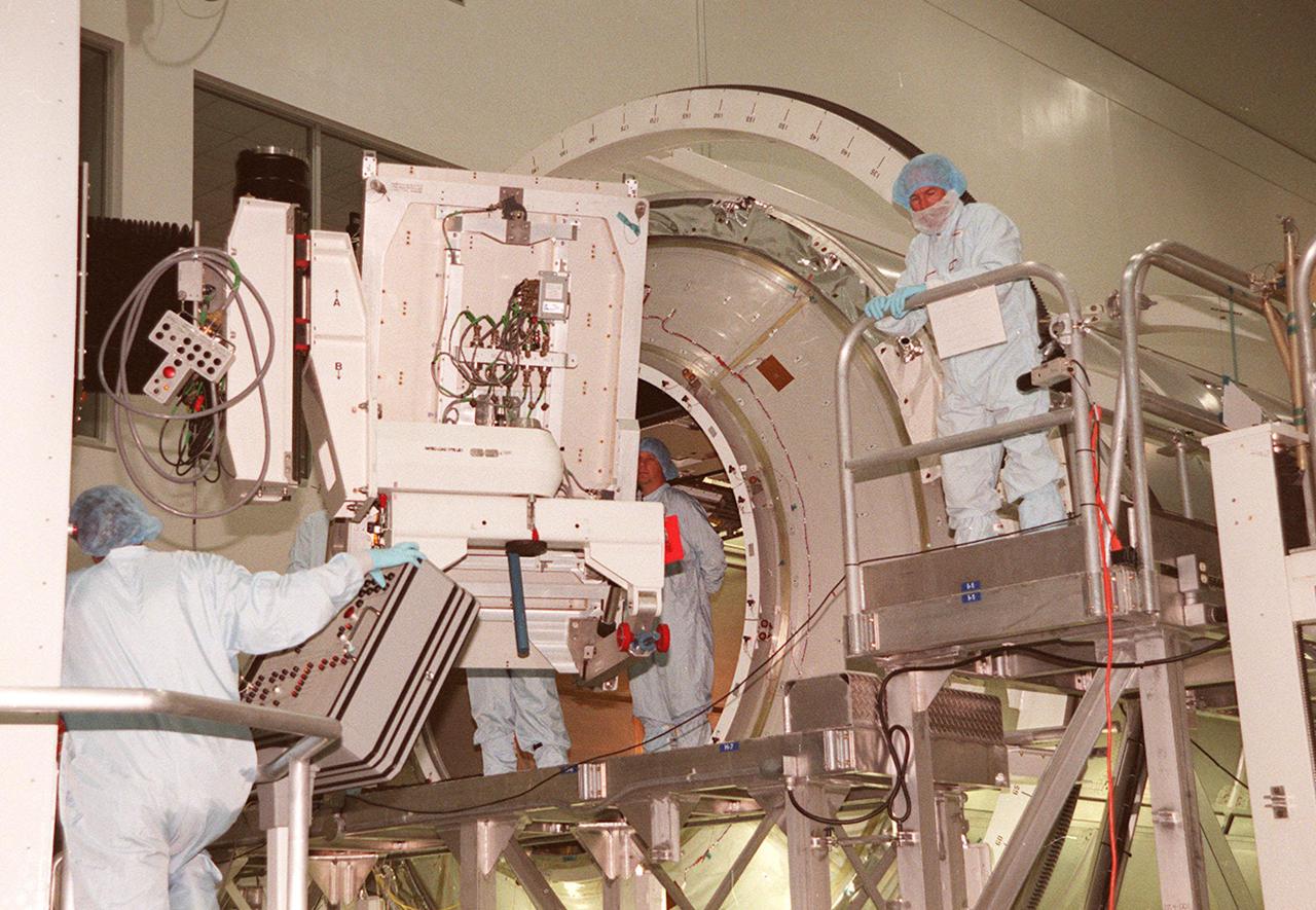 KENNEDY SPACE CENTER, FLA. -- Workers (right, left and center) in the Space Station Processing Facility wait to install a laboratory rack in the Multi-Purpose Logistics Module Leonardo (background). Leonardo is the first of three such pressurized modules that will serve as the International Space Station's “moving vans,” carrying laboratory racks filled with equipment, experiments and supplies to and from the Space Station aboard the Space Shuttle. Approximately 21 feet long and 15 feet in diameter, Leonardo will be launched on Shuttle mission STS-102 March 1, 2001. On that flight, Leonardo will be filled with equipment and supplies to outfit the U.S. laboratory module, being carried to the ISS on the Jan. 19, 2001, launch of STS-98