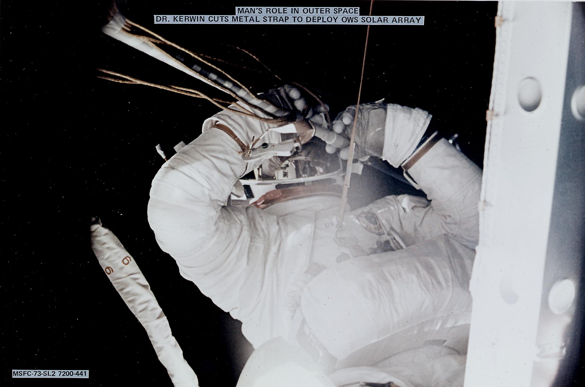 Kerwin cutting the metal strap to free and deploy Skylab's Orbital Workshop solar array