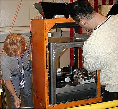 The first NASA Dropping In a Microgravity Environment (DIME) student competition pilot project came to a conclusion at the Glenn Research Center in April 2001. The competition involved high-school student teams who developed the concept for a microgravity experiment and prepared an experiment proposal. The two student teams - COSI Academy, sponsored by the Columbus Center of Science and Industry, and another team from Cincinnati, Ohio's Sycamore High School, designed a microgravity experiment, fabricated the experimental apparatus, and visited NASA Glenn to operate their experiment in the 2.2 Second Drop Tower. Here Carol Hodanbosi of the National Center for Microgravity Research and Jose Carrion, a lab mechanic with AKAC, prepare a student experiment package (inside the silver-colored frame) inside the orange-colored drag shield that encloses all experiment hardware. This image is from a digital still camera; higher resolution is not available.