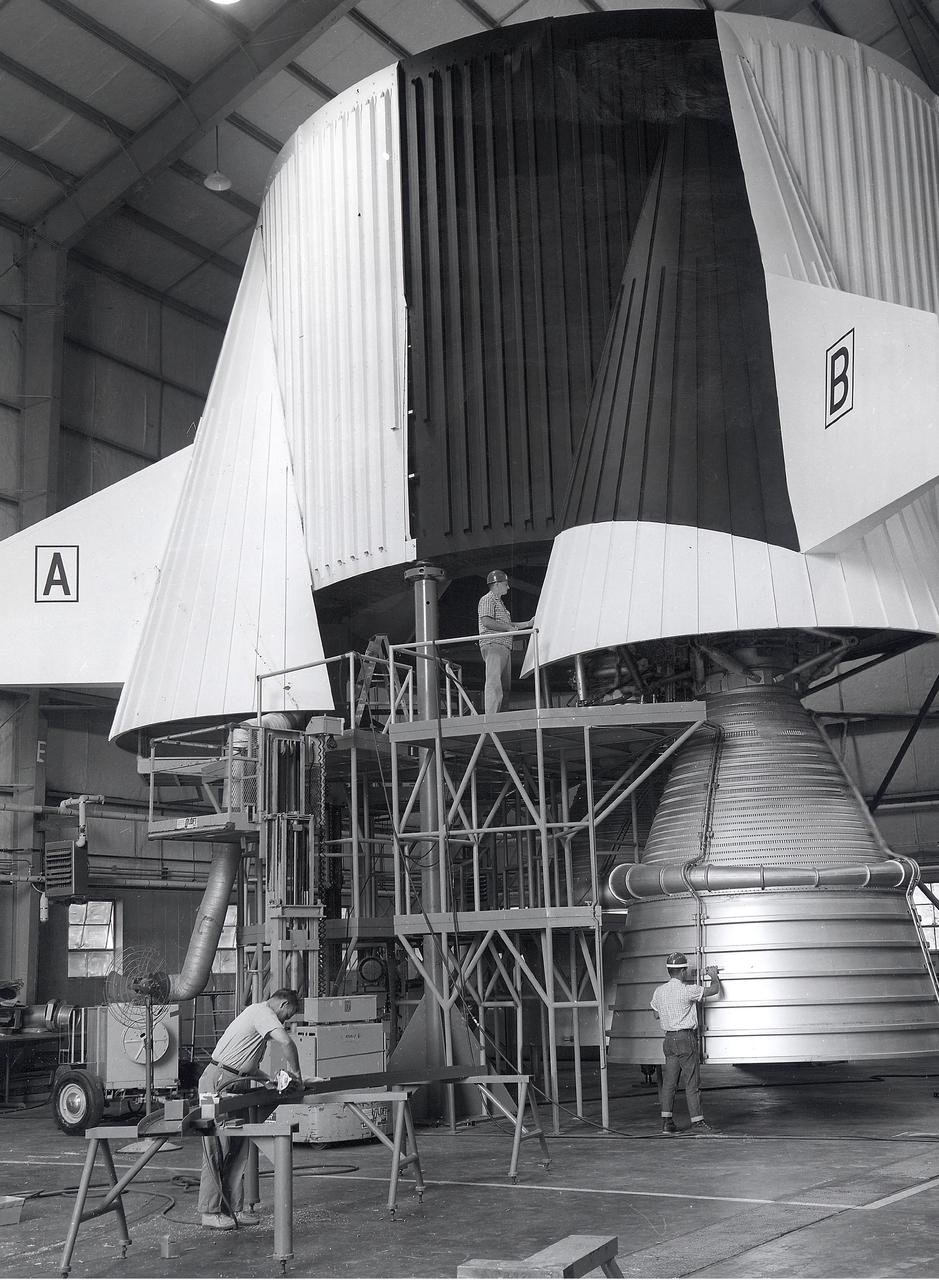 This photograph depicts Marshall Space Flight Center employees, James Reagin, machinist (top); Floyd McGinnis, machinist; and Ernest Davis, experimental test mechanic (foreground), working on a mock up of the S-IC thrust structure. The S-IC stage is the first stage, or booster, of the 364-foot long Saturn V rocket that ultimately took astronauts to the Moon. The  S-IC stage, burned over 15 tons of propellant per second during its 2.5 minutes of operation to take the vehicle to a height of about 36 miles and to a speed of about 6,000 miles per hour. The stage was 138 feet long and 33 feet in diameter. Operating at maximum power, all five of the engines produced 7,500,000 pounds of thrust. 