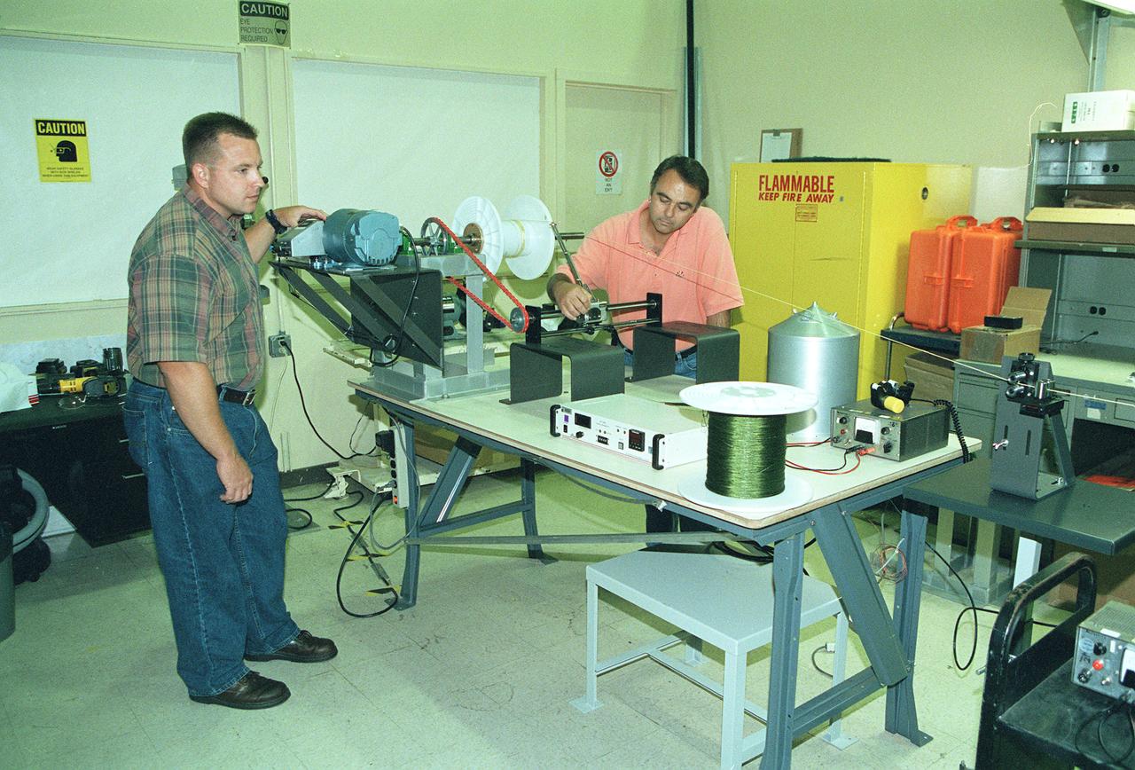This photograph shows two Marshall Space Flight Center (MSFC) engineers, Mark Vaccaro (left) and Ken Welzyn, testing electrodynamic tethers in the MSFC Tether Winding and Spark Testing Facility. For 4 years, MSFC and industry partners have been developing the Propulsive Small Expendable Deployer System experiment, called ProSEDS. ProSEDS will test electrodynamic tether propulsion technology. Electrodynamic tethers are long, thin wires that collect electrical current when passing through a magnetic field. The tether works as a thruster as a magnetic field exerts a force on a current-carrying wire. Since electrodynamic tethers require no propellant, they could substantially reduce the weight of the spacecraft and provide a cost-effective method of reboosting spacecraft. The initial flight of ProSEDS is scheduled to fly aboard an Air Force Delta II rocket in the summer of 2002. In orbit, ProSEDS will deploy from a Delta II second stage. It will be a 3.1-mile (5 kilometer) long, ultrathin base-wire tether cornected with a 6.2-mile (10 kilometer) long non-conducting tether. This photograph shows Less Johnson, a scientist at MSFC, inspecting the nonconducting part of a tether as it exits a deployer similar to the one to be used in the ProSEDS experiment. The ProSEDS experiment is managed by the Space Transportation Directorate at MSFC.