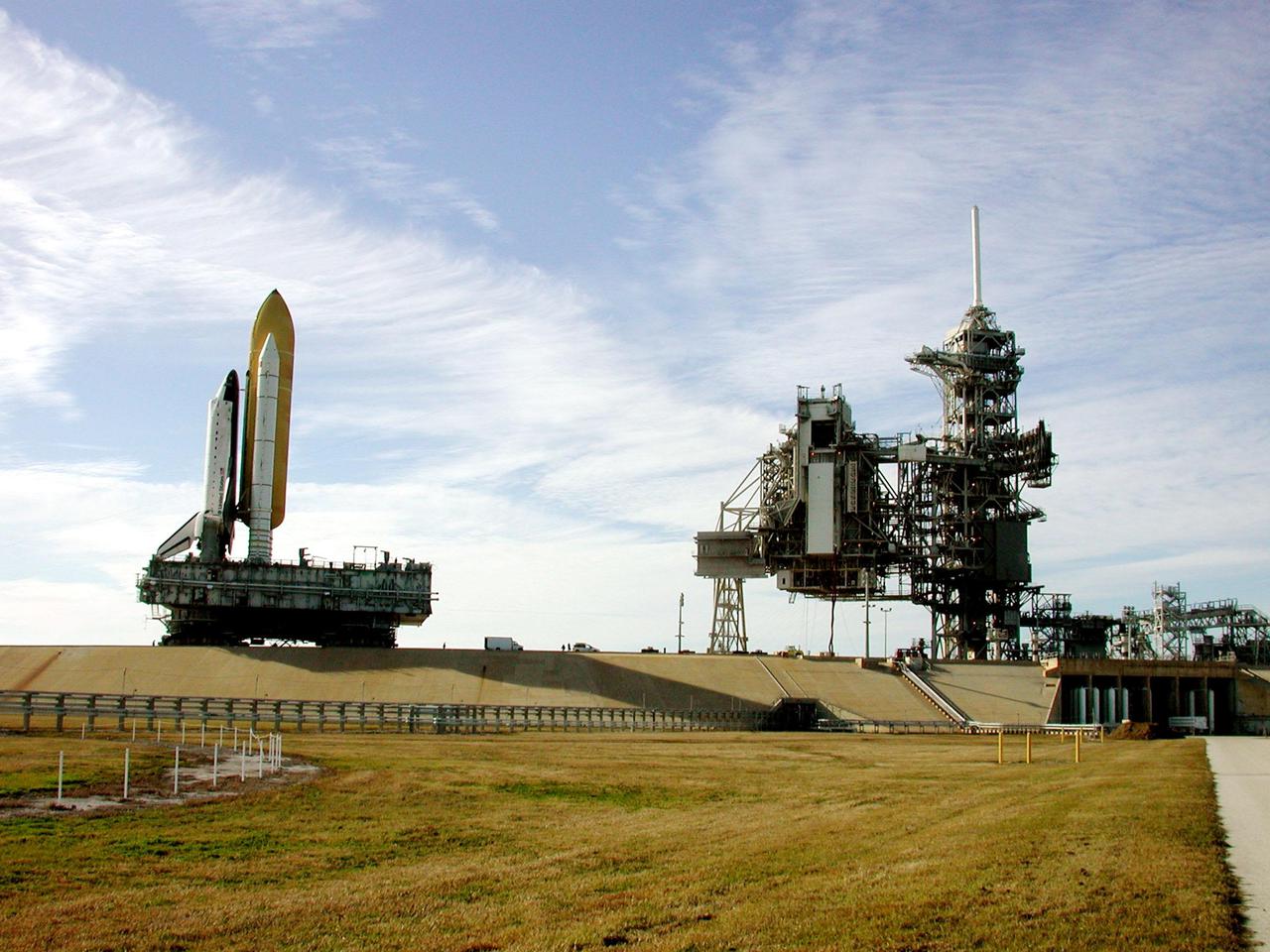 KENNEDY SPACE CENTER, Fla. -- Under wispy white morning clouds, Space Shuttle Atlantis approaches Launch Pad 39A, which shows the Rotating Service Structure open (left) and the Fixed Service Structure (right). At the RSS, the payload canister is being lifted up to the Payload Changeout Room. This is the Shuttle’s second attempt at rollout. Jan. 2 a failed computer processor on the crawler transporter aborted the rollout and the Shuttle was returned to the Vehicle Assembly Building using a secondary computer processor on the vehicle. Atlantis will fly on mission STS-98, the seventh construction flight to the International Space Station, carrying the U.S. Laboratory, named Destiny. The lab will have five system racks already installed inside the module. After delivery of electronics in the lab, electrically powered attitude control for Control Moment Gyroscopes will be activated. Atlantis is scheduled for launch no earlier than Jan. 19, 2001, with a crew of five