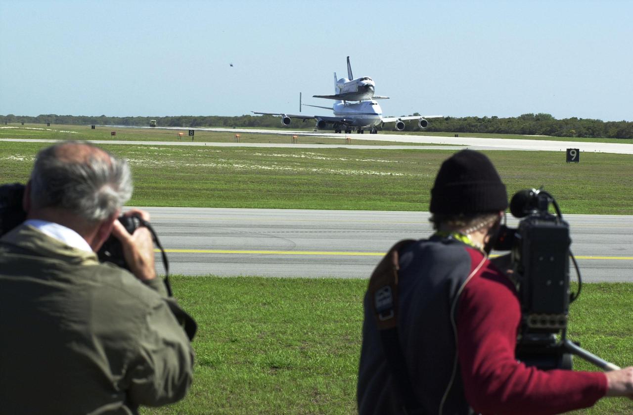KENNEDY SPACE CENTER, FLA. -- Media (foreground) capture the landing of the orbiter Columbia atop a Shuttle Carrier Aircraft. The SCA and its cargo landed at the Cape Canaveral Air Force Station Skid Strip. The ferry flight began in California March 1. Unfavorable weather conditions kept it on the ground at Dyess AFB, Texas, until it could return to Florida. Columbia is returning from a 17-month-long modification and refurbishment process as part of a routine maintenance plan. The orbiter will next fly on mission STS-107, scheduled Oct. 25