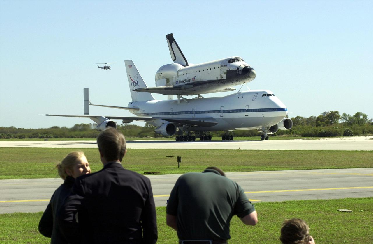 KENNEDY SPACE CENTER, FLA. -- Media (foreground) capture the orbiter Columbia atop a Shuttle Carrier Aircraft as it taxis down the runway. A helicopter hovers in the background. The SCA and its cargo landed at the Cape Canaveral Air Force Station Skid Strip. The ferry flight began in California March 1. Unfavorable weather conditions kept it on the ground at Dyess AFB, Texas, until it could return to Florida. Columbia is returning from a 17-month-long modification and refurbishment process as part of a routine maintenance plan. The orbiter will next fly on mission STS-107, scheduled Oct. 25