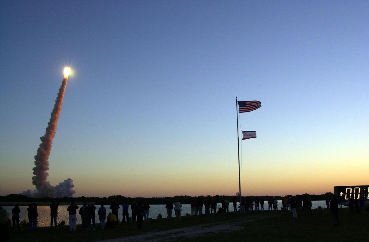 KENNEDY SPACE CENTER, Fla. -- Dozens of spectators line up by the turn basin to watch Space Shuttle Discovery blast off on mission STS-102, the eighth construction flight to the International Space Station. The lower smoke plumes appear red from the dawn’s rays. Liftoff occurred on time at 6:42:09 EST