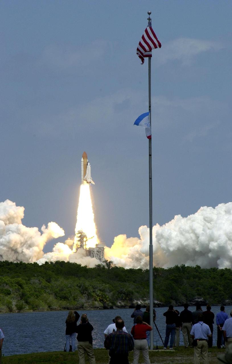 KENNEDY SPACE CENTER, FLA. -- Through a cloud-brushed blue sky, Space Shuttle Endeavour is hurled into space on mission STS-100. Photographers crowd the bank of the turn basin near the flag pole to capture the image on film and video. Liftoff occurred at 2:40:42 p.m. EDT on the ninth flight to the International Space Station. The 11-day mission will deliver and integrate the Spacelab Logistics Pallet_Launch Deployment Assembly, which includes the Space Station Remote Manipulator System and the UHF Antenna. The mission includes two planned spacewalks for installation of the SSRMS on the Station. Also onboard is the Multi-Purpose Logistics Module Raffaello, carrying resupply stowage racks and resupply_return stowage platforms