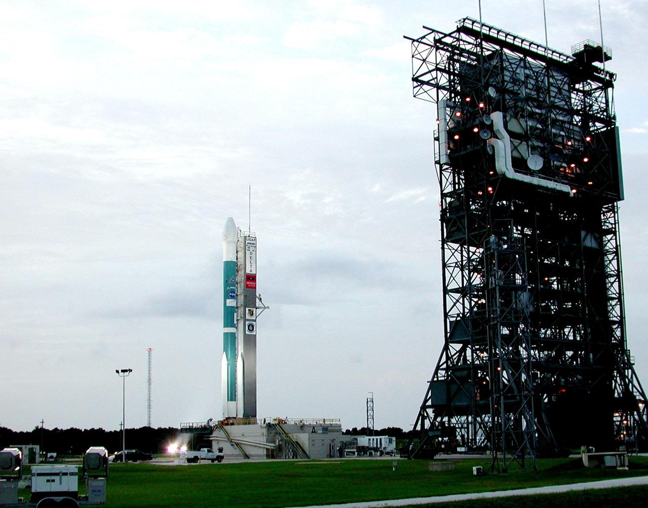 KENNEDY SPACE CENTER, Fla. -- After rollback of the Mobile Service Tower (right), the Delta II rocket with the Genesis spacecraft on top sits on Launch Complex 17-A, Cape Canaveral Air Force Station, ready for liftoff. A gray overcast sky forecasts a questionable launch effort due to weather conditions. Genesis will be on a robotic NASA space mission to collect just 10 to 20 micrograms -- or the weight of a few grains of salt -- of solar wind, invisible charged particles that flow outward from the Sun -- and return them to Earth. This treasured smidgen of the Sun will be preserved in a special laboratory for study by scientists over the next century in search of answers to fundamental questions about the exact composition of our star and the birth of our solar system. The Genesis launch is scheduled for Aug. 1, 2001, from CCAFS