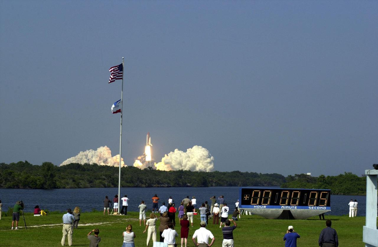 KENNEDY SPACE CENTER, Fla. -- Spectators gather on the grounds in front of the bleachers at the turn basin to watch the launch of Space Shuttle Discovery. A breeze from the southeast that has the flags snapping also kept gathering clouds away for the on-time liftoff at 5:10:14 p.m. EDT. Besides the Shuttle crew of four, Discovery carries the Expedition Three crew who will replace Expedition Two on the International Space Station. The mission includes the third flight of an Italian-built Multi-Purpose Logistics Module delivering additional scientific racks, equipment and supplies for the Space Station, and two spacewalks. Part of the payload is the Early Ammonia Servicer (EAS) tank, which will be attached to the Station during the spacewalks. The EAS will be installed on the P6 truss, which holds the Station’s giant U.S. solar arrays, batteries and the cooling radiators. The EAS contains spare ammonia for the Station’s cooling system. The three-member Expedition Two crew will be returning to Earth aboard Discovery after a five-month stay on the Station