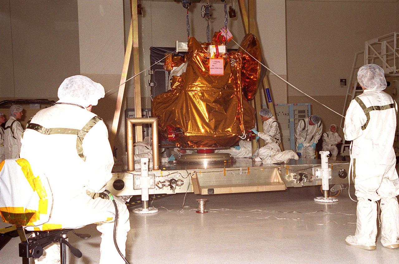 The <a href=http:__mars.jpl.nasa.gov_2001_>2001 Mars Odyssey Orbiter <_a>comes to rest on a workstand in the Spacecraft Assembly and Encapsulation Facility -2. Workers check the spacecraft’s position. The Mars Odyssey Orbiter carries three science instruments: the Thermal Emission Imaging System (THEMIS), the Gamma Ray Spectrometer (GRS), and the Mars Radiation Environment Experiment (MARIE). THEMIS will map the mineralogy and morphology of the Martian surface using a high-resolution camera and a thermal infrared imaging spectrometer. The GRS will achieve global mapping of the elemental composition of the surface and determine the abundance of hydrogen in the shallow subsurface. [The GRS is a rebuild of the instrument lost with the Mars Observer mission.] The MARIE will characterize aspects of the near-space radiation environment as related to the radiation-related risk to human explorers. The Mars Odyssey Orbiter is scheduled for launch on April 7, 2001, aboard a Delta 7925 rocket from Launch Pad 17-A, Cape Canaveral Air Force Station