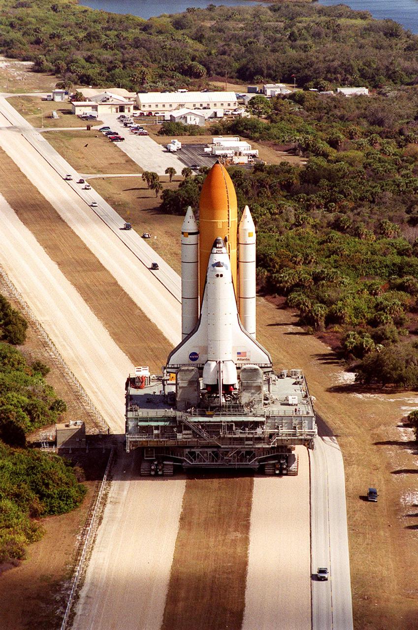 KENNEDY SPACE CENTER, FLA. -- On its way back from <a href='http:__www-pao.ksc.nasa.gov_kscpao_captions_subjects_lc39a.htm'>Launch Pad 39A,<_a> Space Shuttle <a href='http:__www-pao.ksc.nasa.gov_kscpao_captions_subjects_atlantis.htm'> Atlantis<_a>, towering above the vehicles on the adjacent road, makes the turn on the crawlerway leading to the <a href='http:__www-pao.ksc.nasa.gov_kscpao_captions_subjects_vab.htm'> Vehicle Assembly Building. <_a>In the VAB workers will conduct inspections, make continuity checks and conduct X-ray analysis on the 36 solid rocket booster cables located inside each booster’s external system tunnel. An extensive evaluation of NASA’s SRB cable inventory revealed conductor damage in four (of about 200) cables on the shelf. Shuttle managers decided to prove the integrity of the system tunnel cables already on Atlantis. The launch has been rescheduled no earlier than Feb. 6